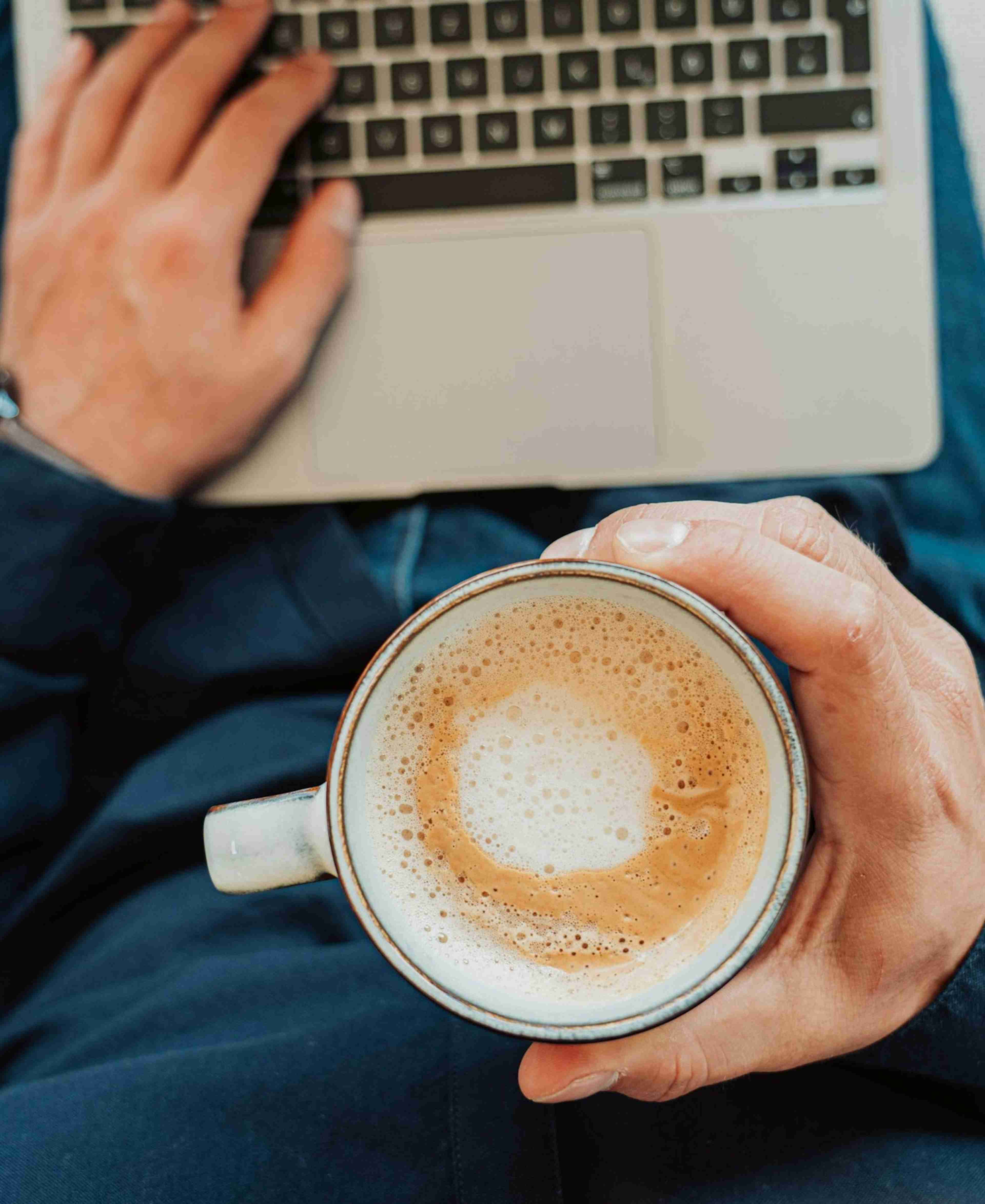 Man holding white ceramic mug with coffee in it whilst working on a MacBook Air