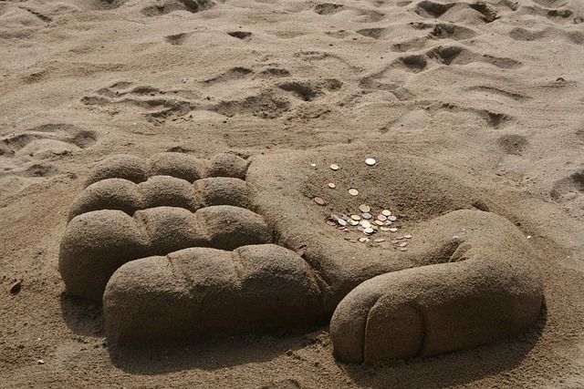 Sand design ‘hand castle’ with money in the palm of the hand