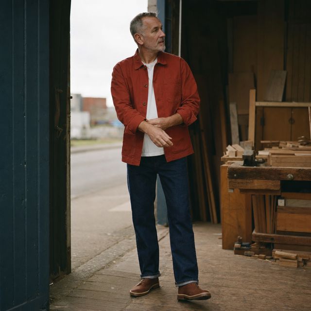 Brick-red canvas chore jacket in a joinery workshop doorway