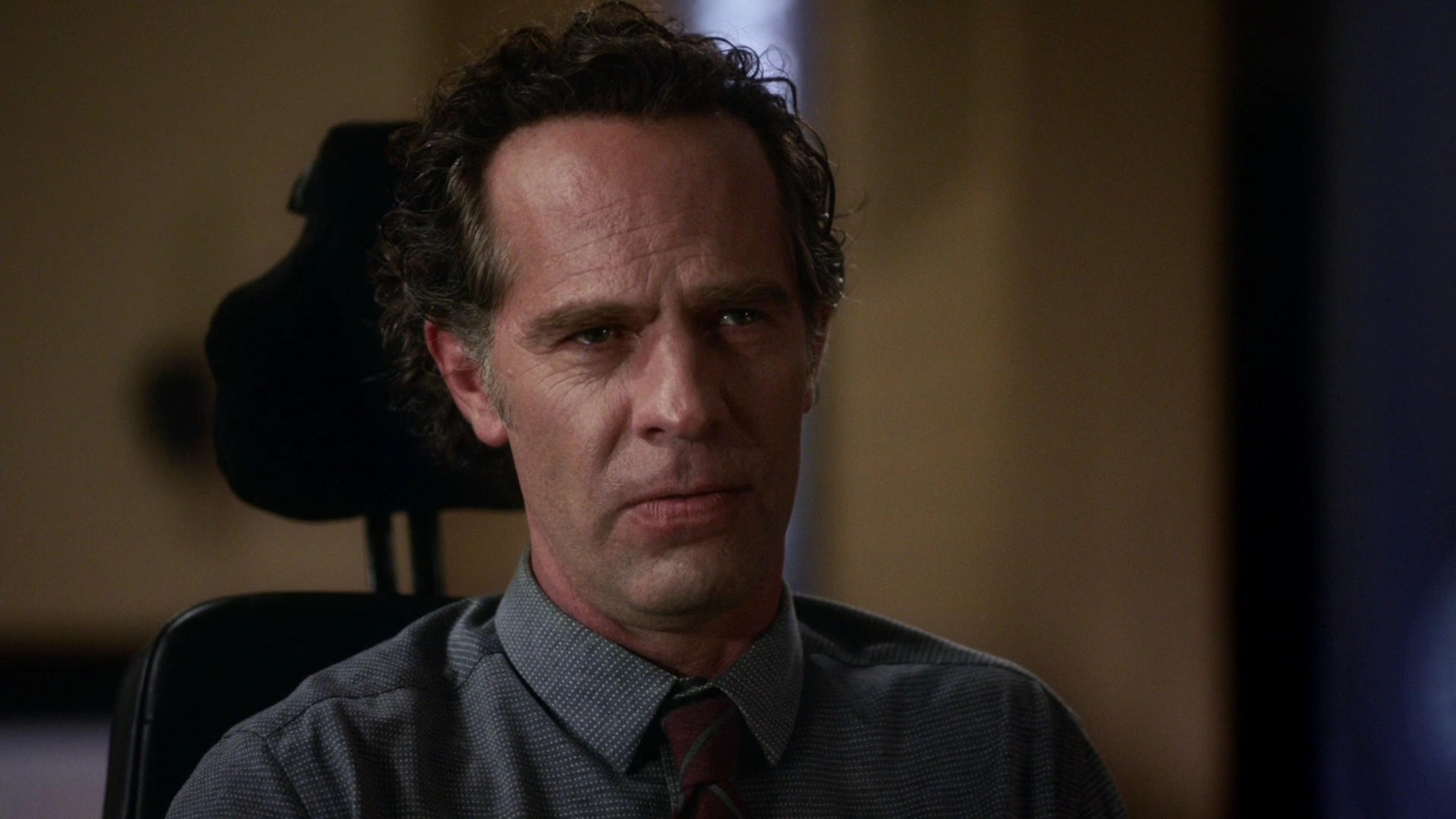 A middle-aged man in a gray suit and tie, with a serious expression