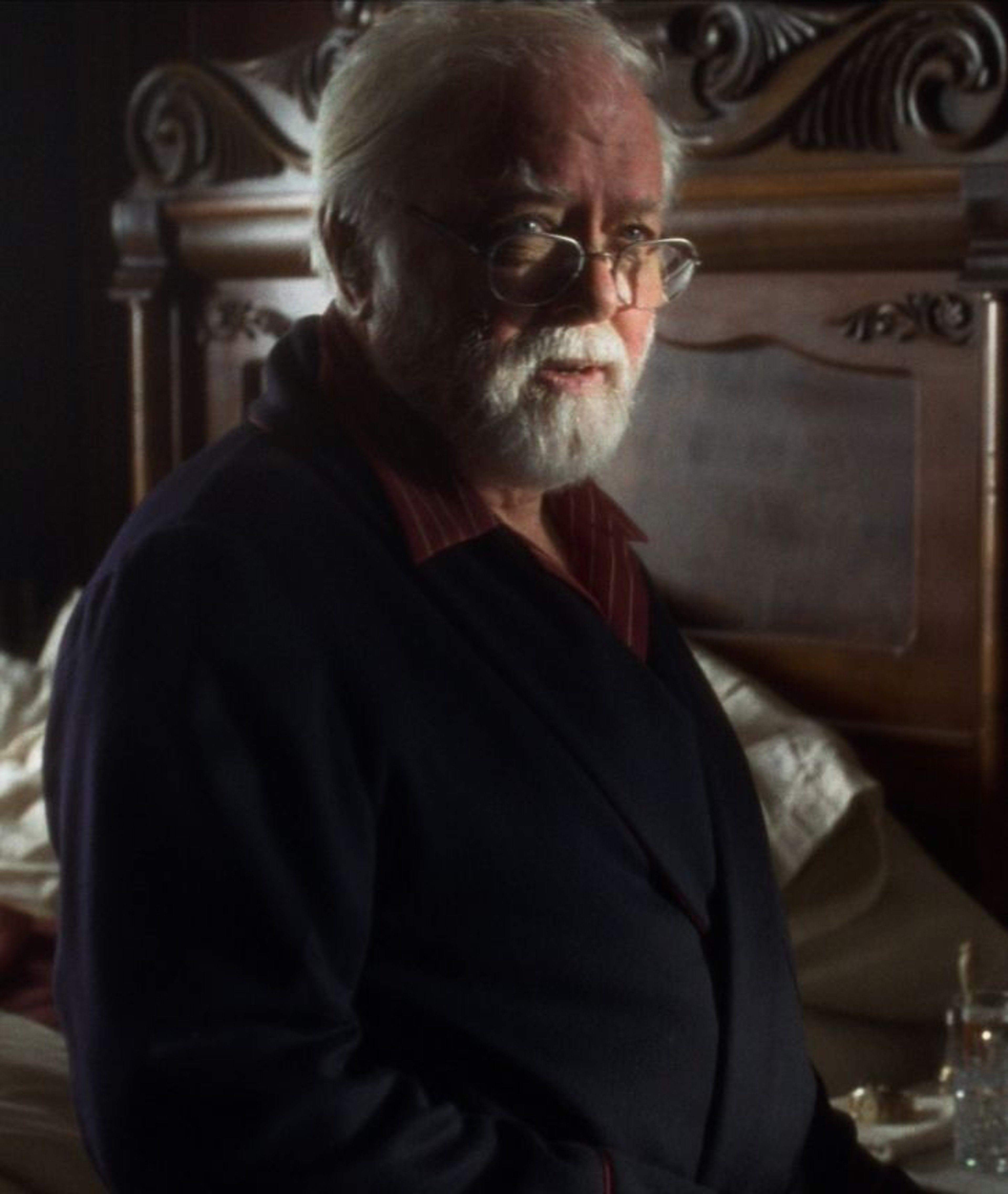 An elderly man with a white beard and glasses, wearing a dark jacket and looking thoughtful.