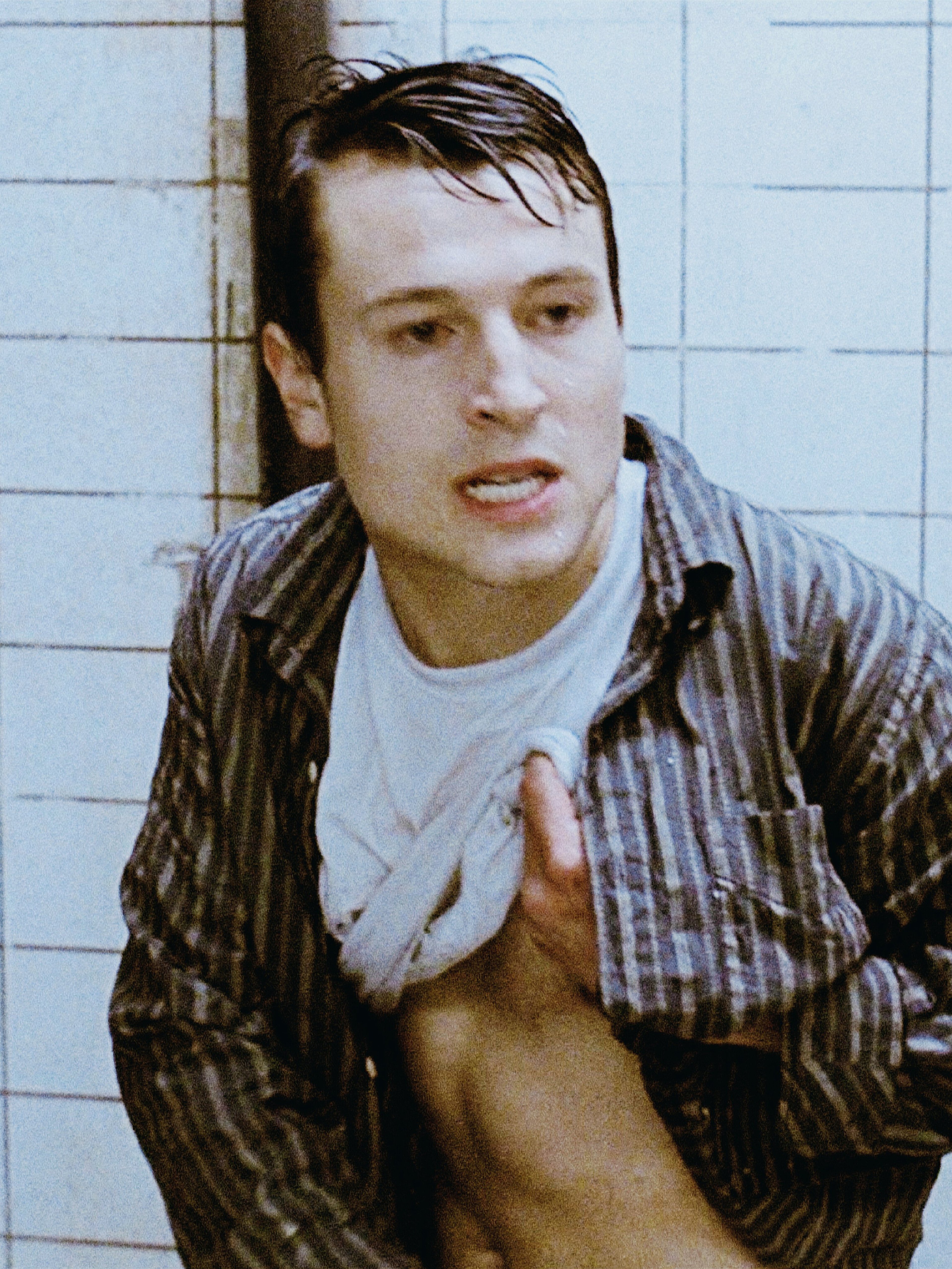 A young man with short dark hair and a slightly disheveled appearance, wearing a plaid shirt and looking concerned or anxious.