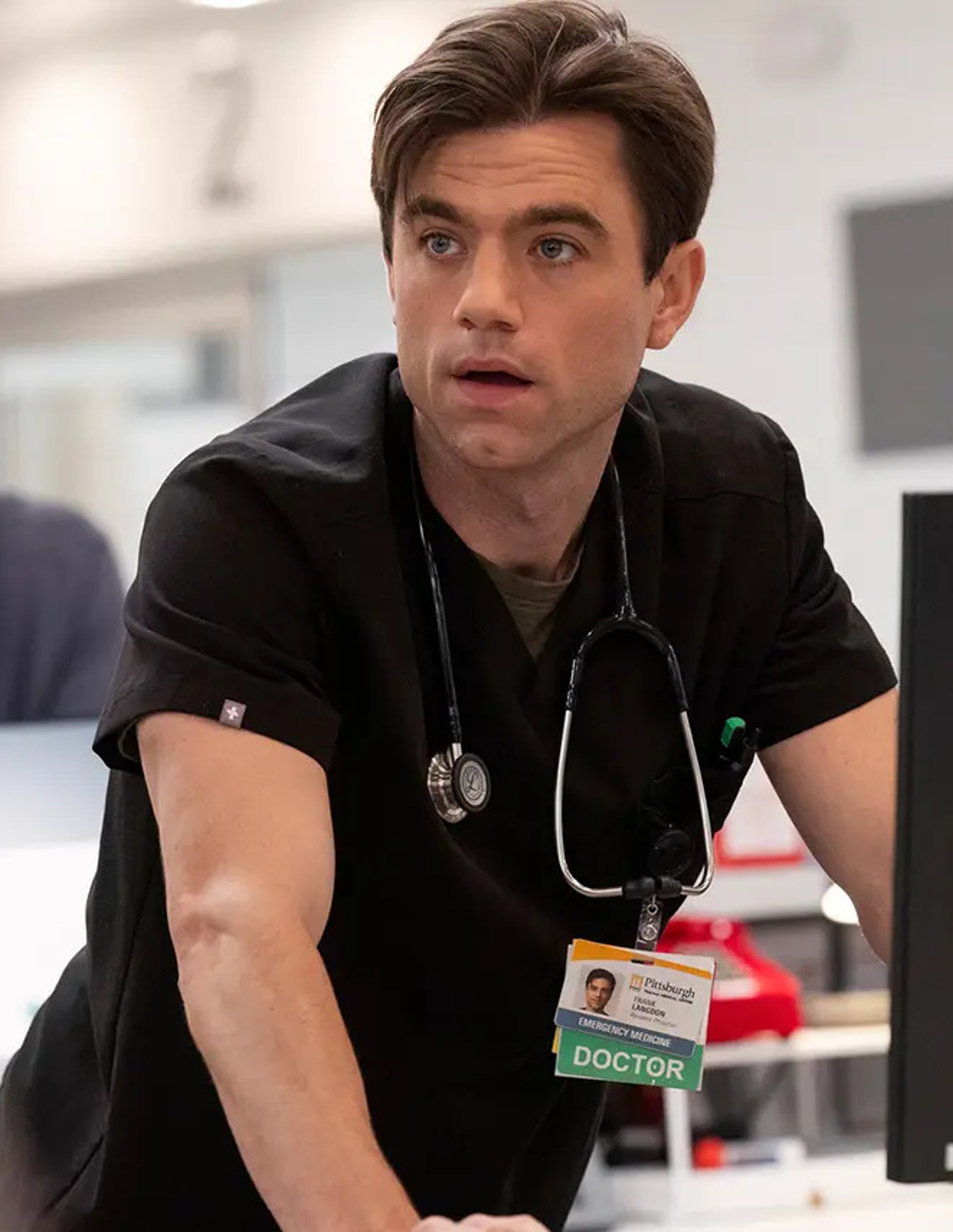 A man in medical scrubs with a stethoscope, looking serious