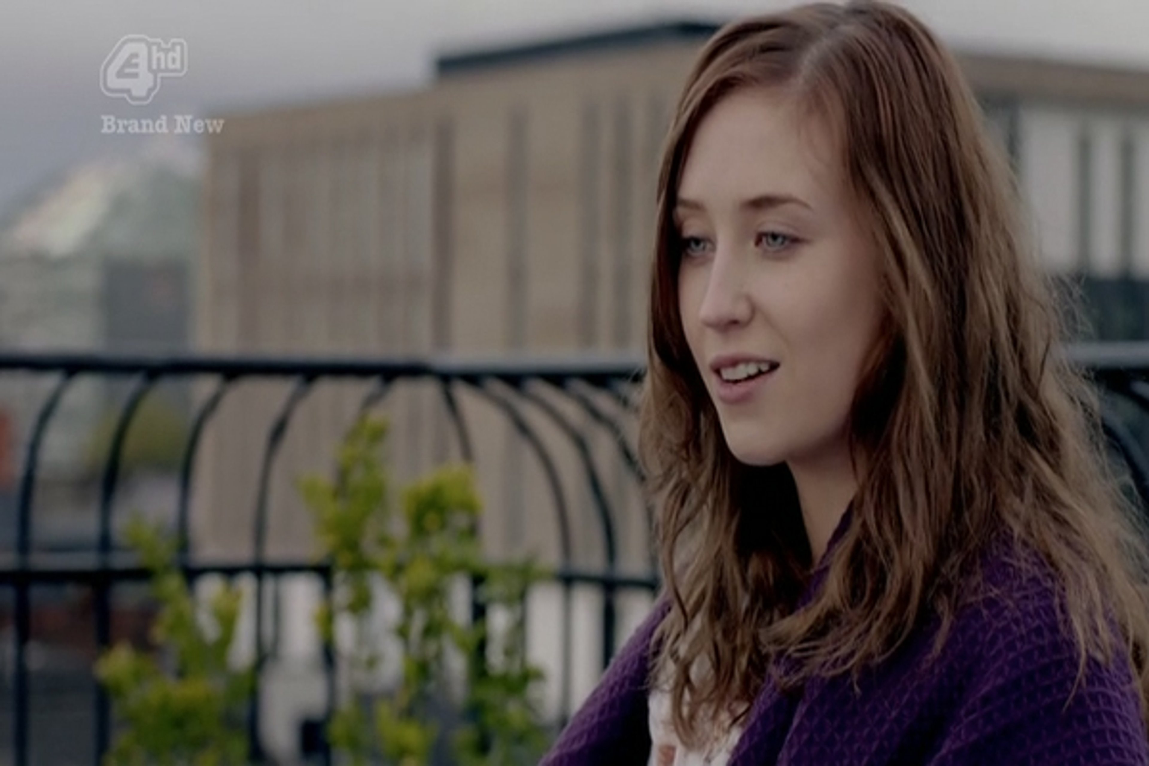 A young woman with long brown hair and a purple jacket smiling at the camera.