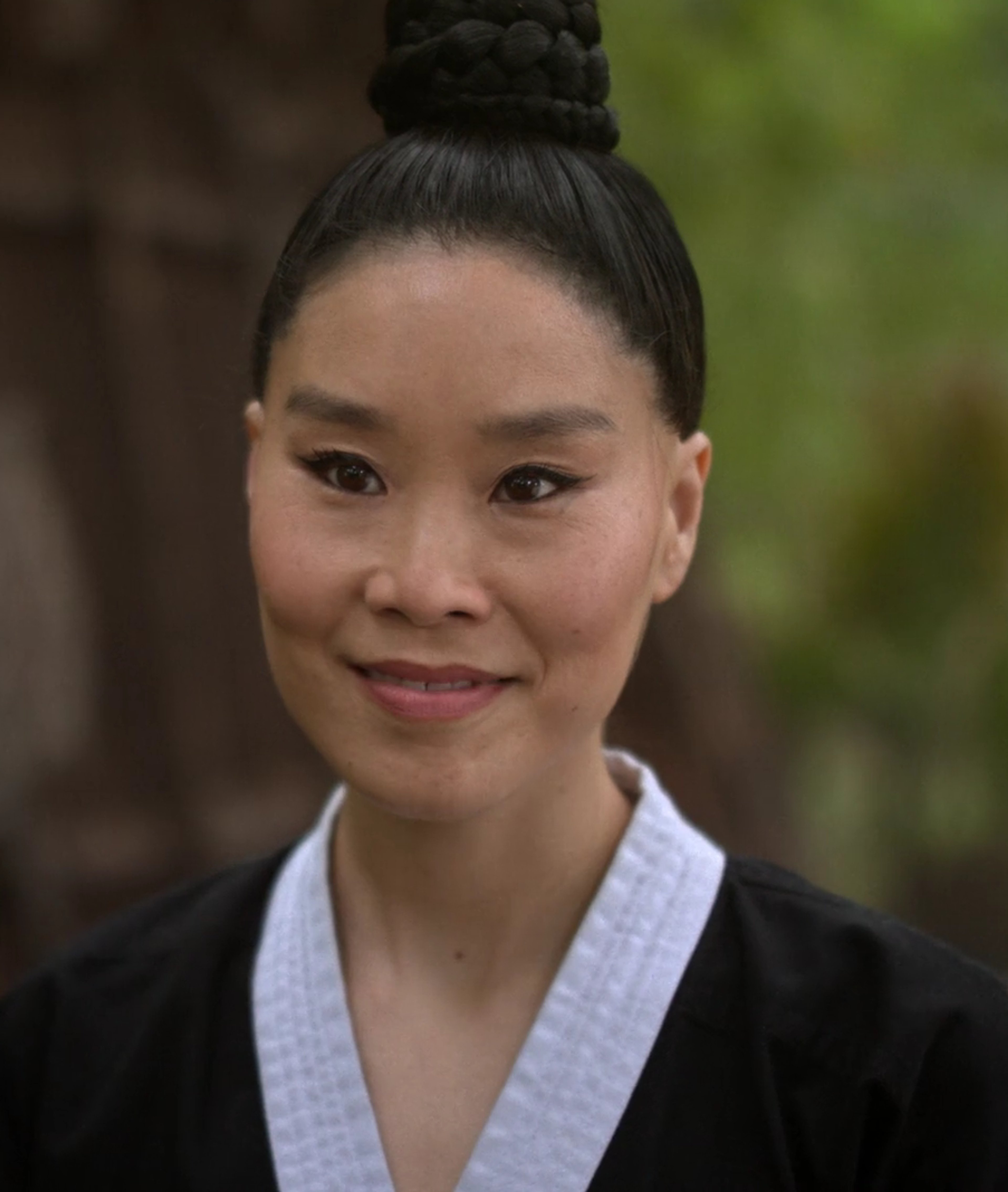 A woman in a white martial arts uniform with her hair in a bun, looking directly at the camera with a serious expression.
