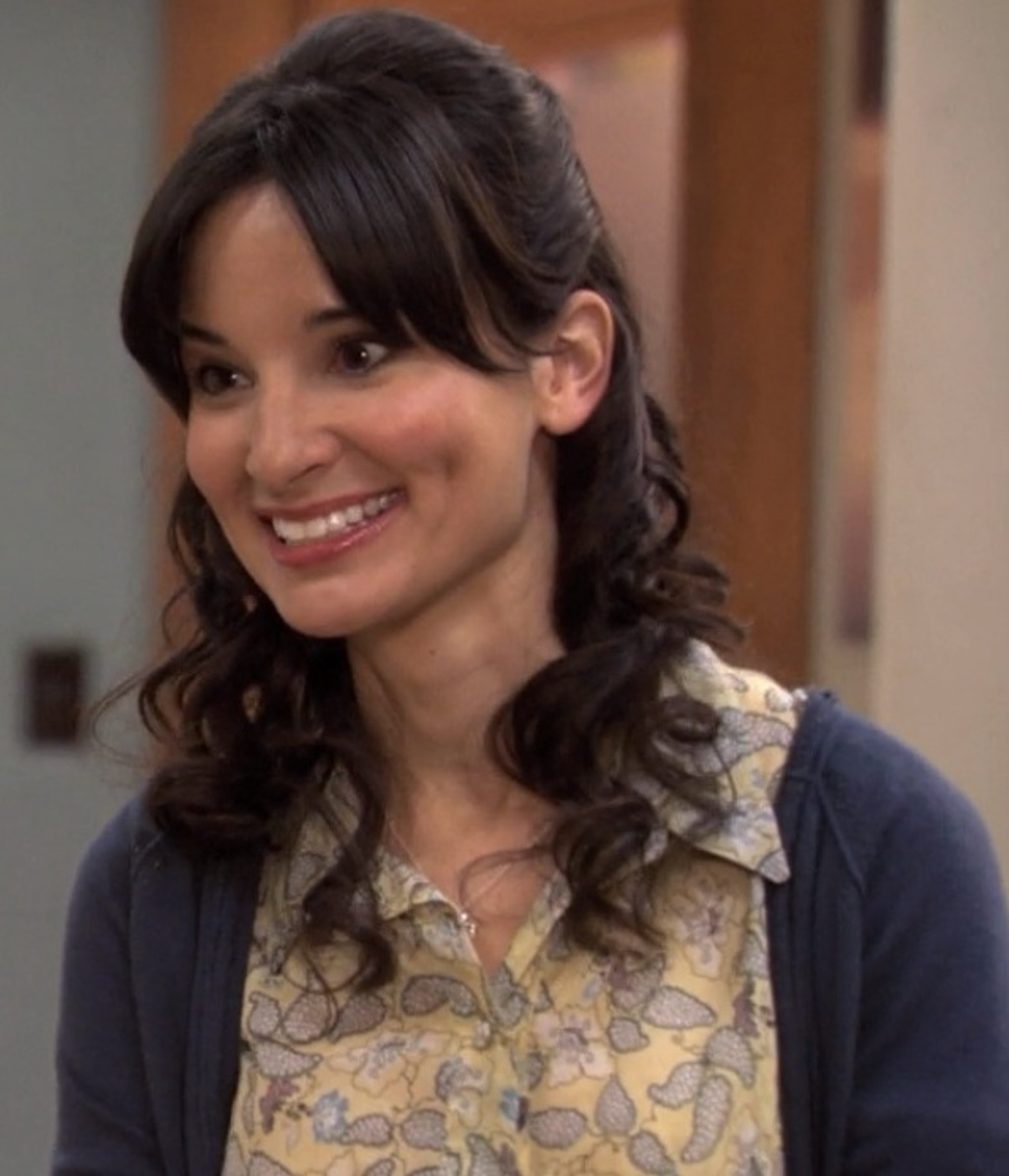 A smiling young woman with long dark hair wearing a floral print blouse