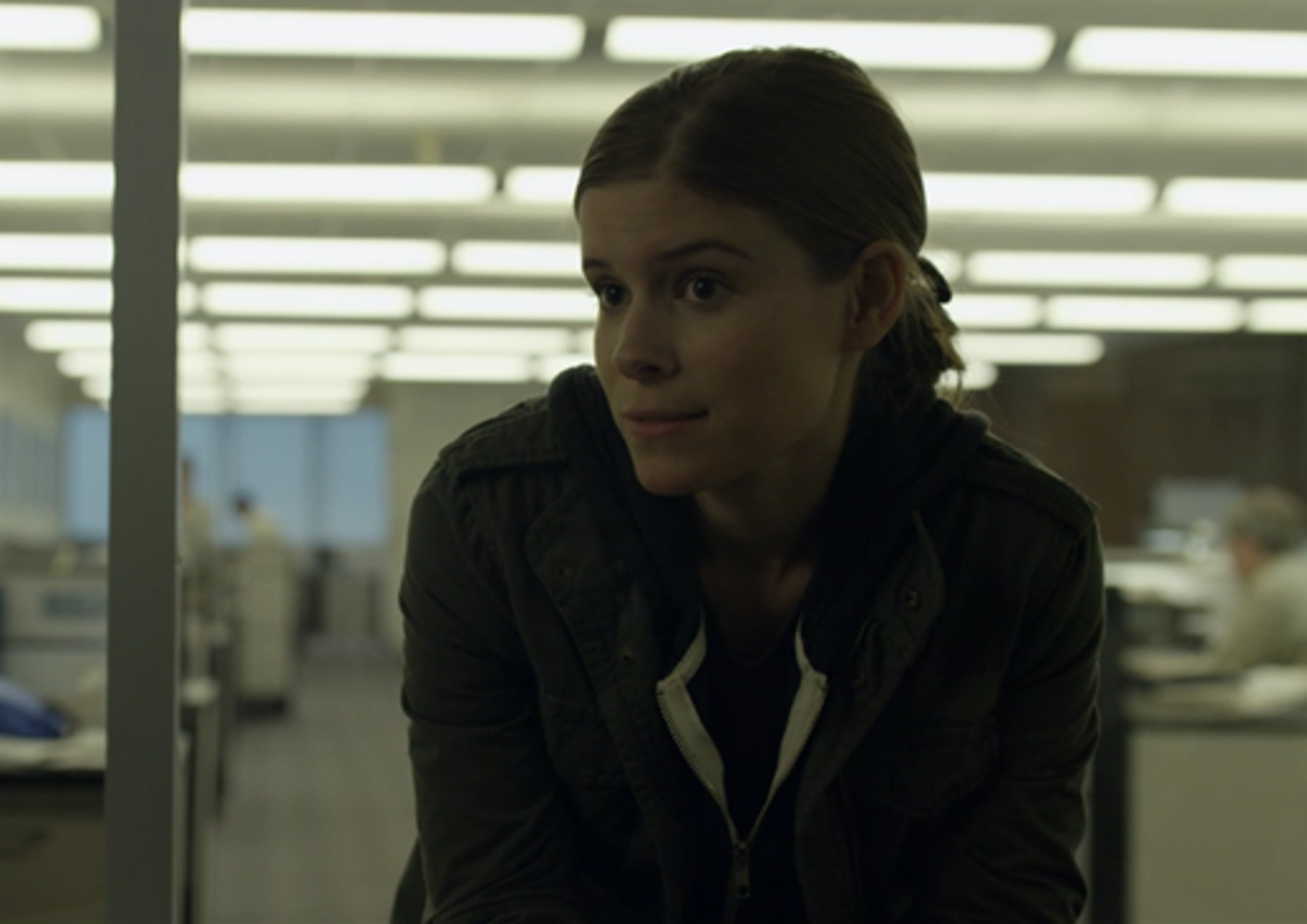 A young woman with dark hair in a serious expression, in an office setting.