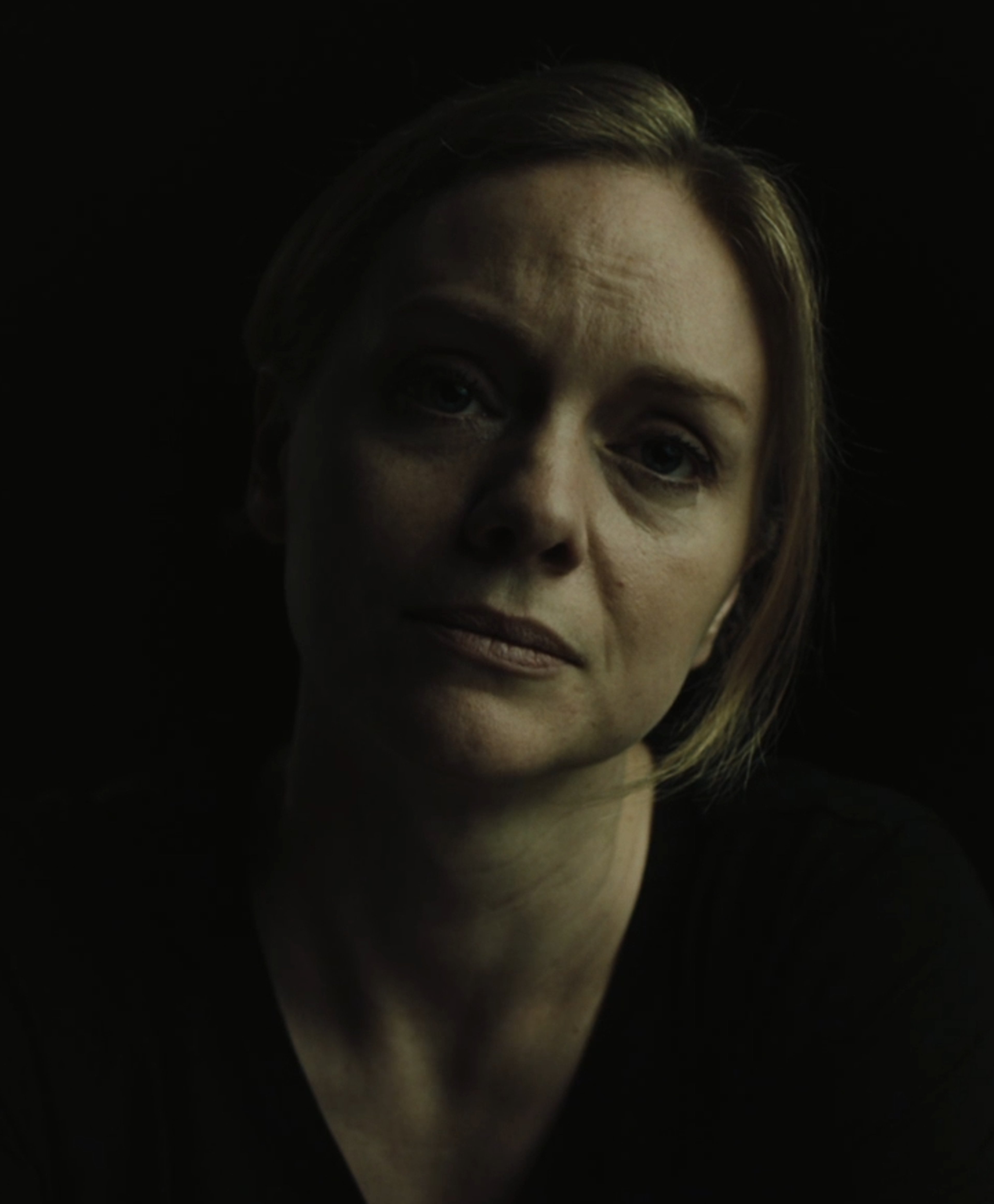 A close-up portrait of a serious-looking middle-aged woman with short, dark hair