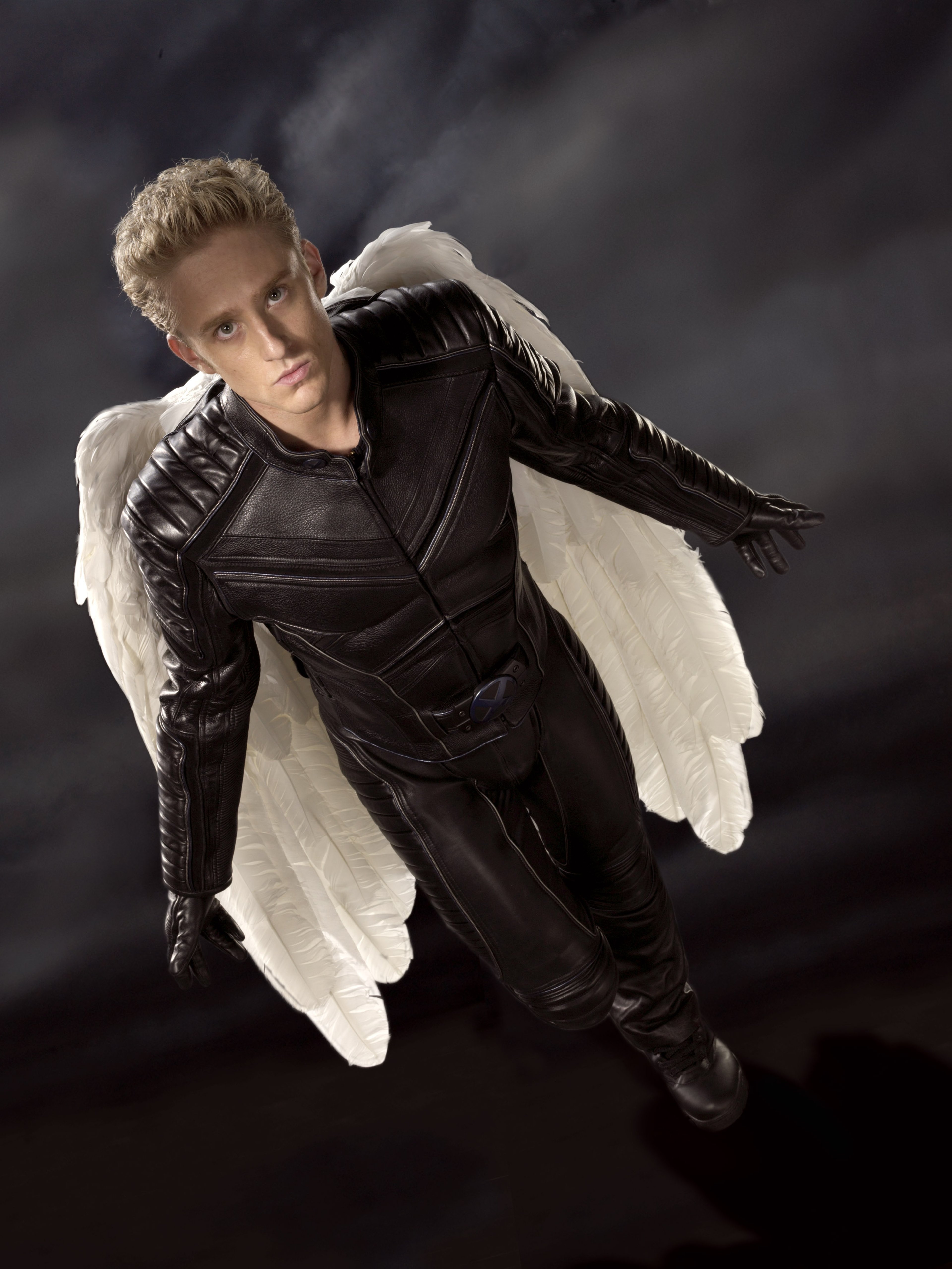 A young man with large white wings extending from his back, wearing a black leather jacket and pants.