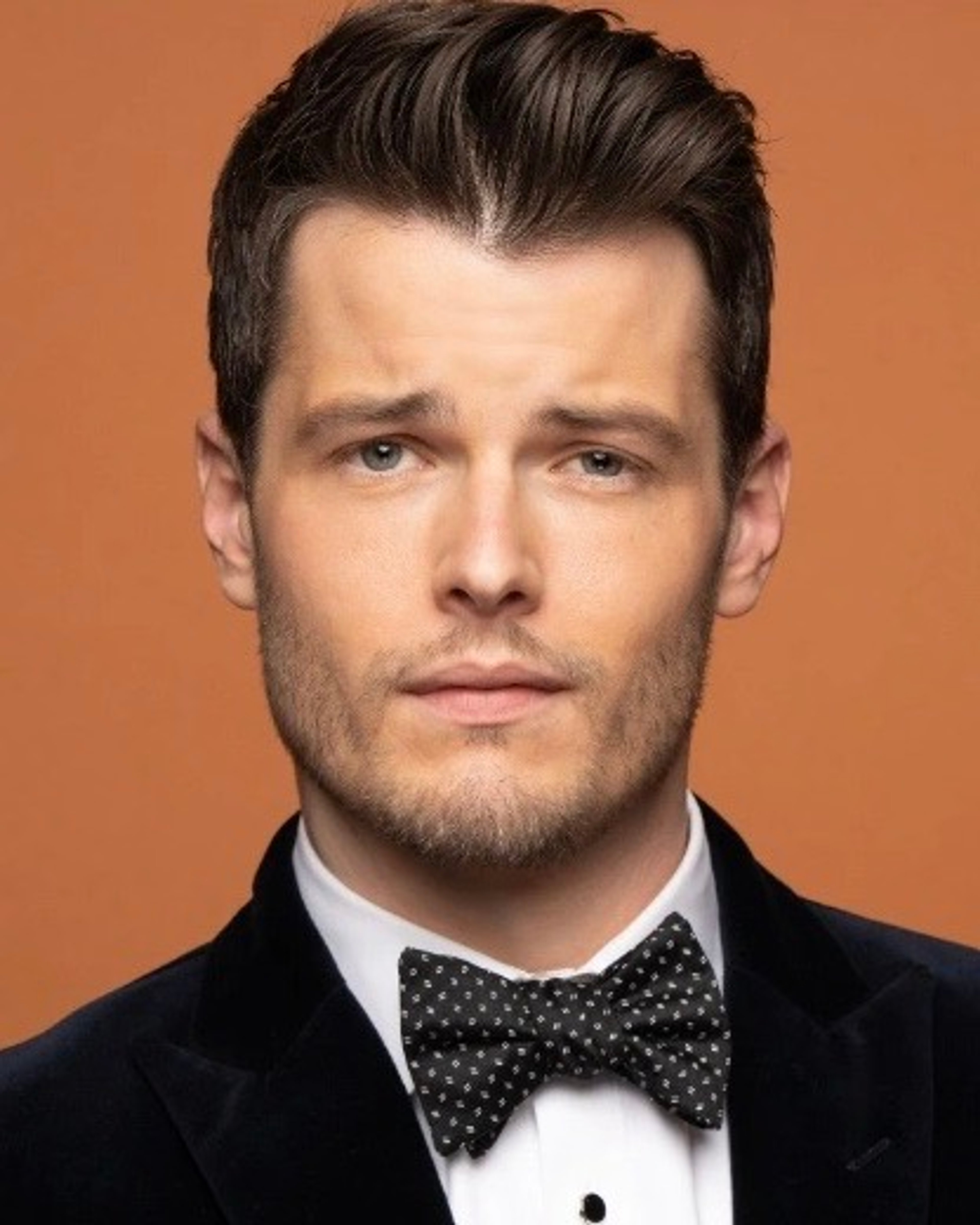 A well-dressed young man in a tuxedo with a serious expression