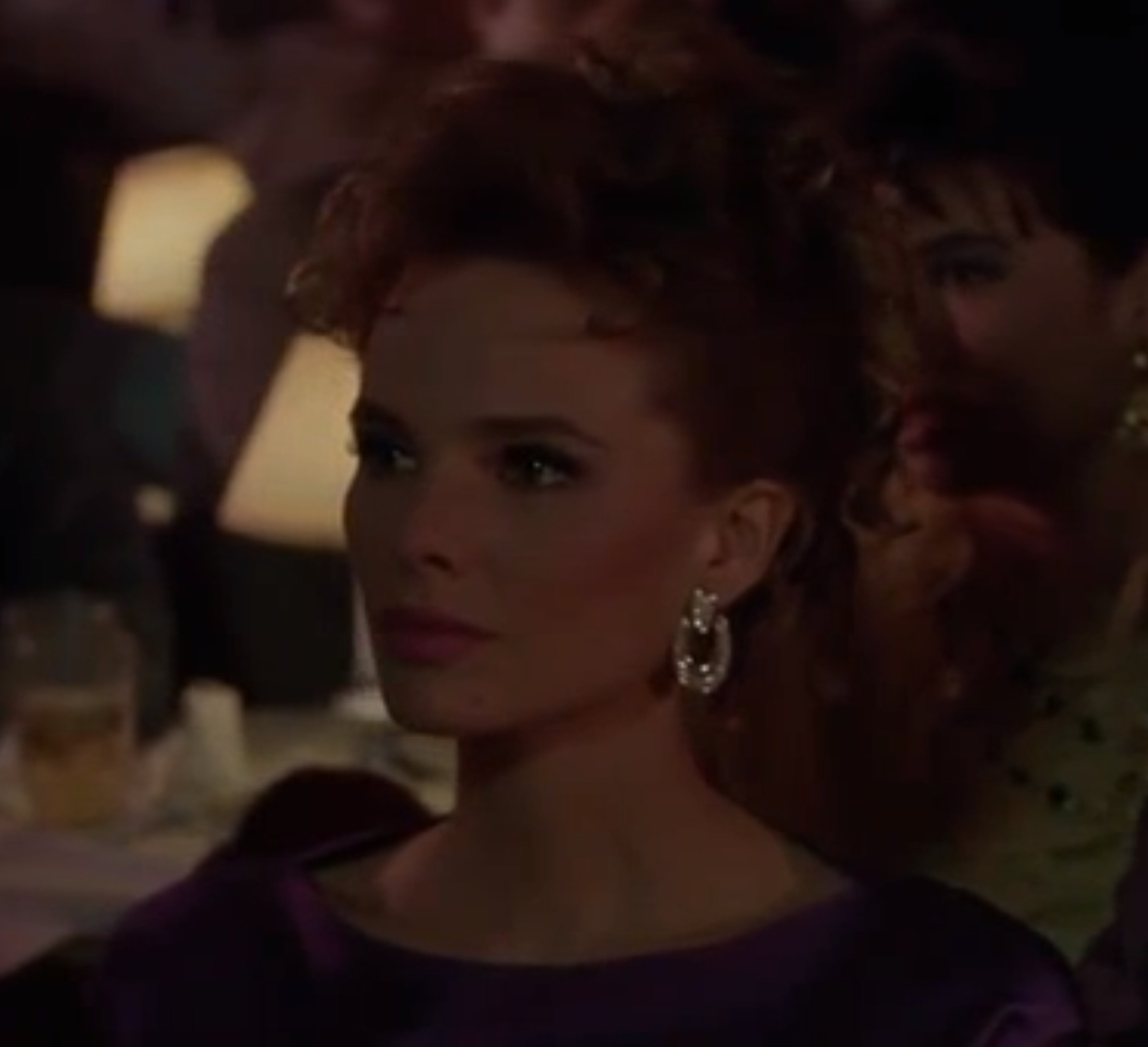 A woman with curly dark hair wearing a purple dress in a dimly lit setting