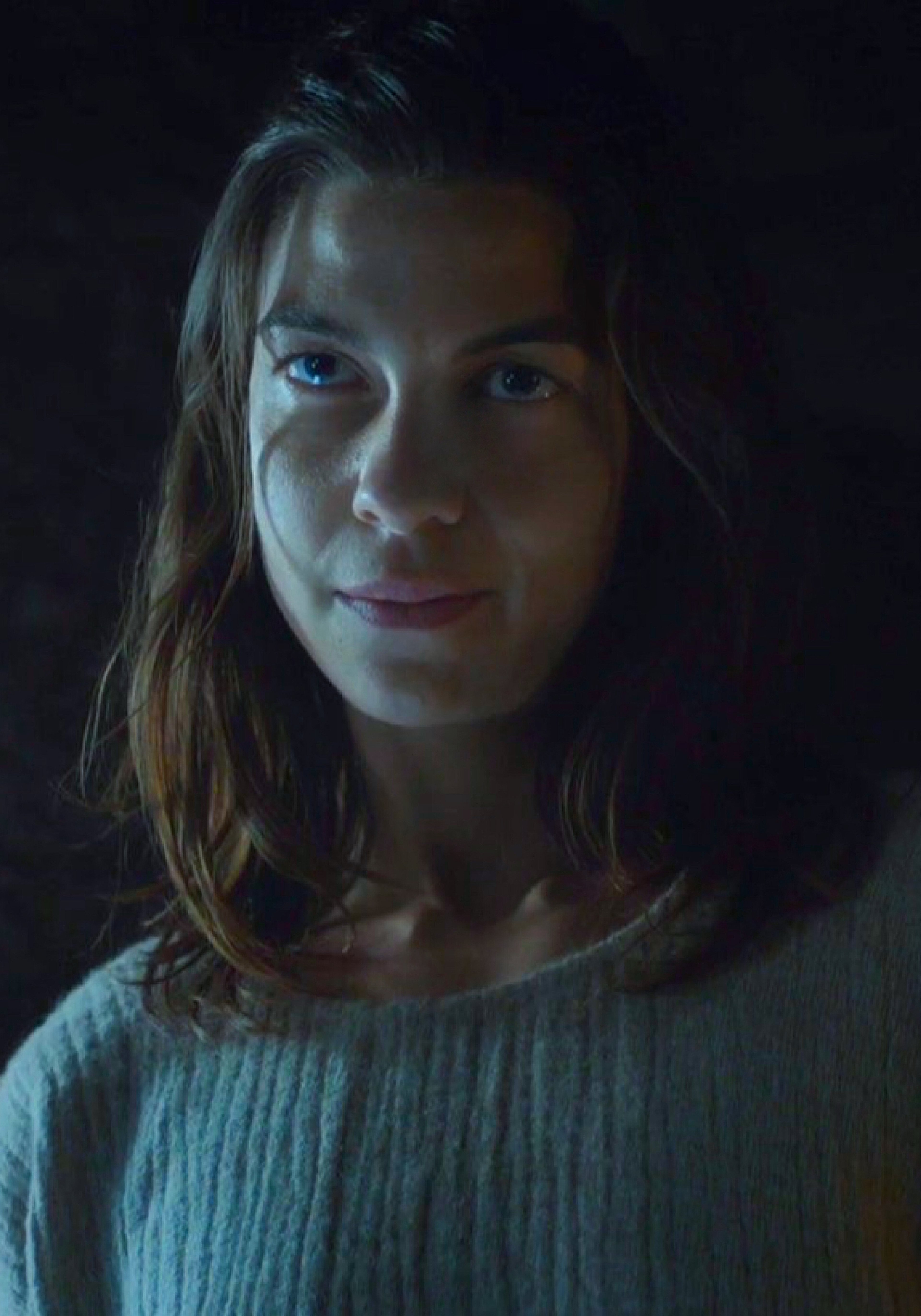 A young woman with blonde hair and blue eyes in a dimly lit setting