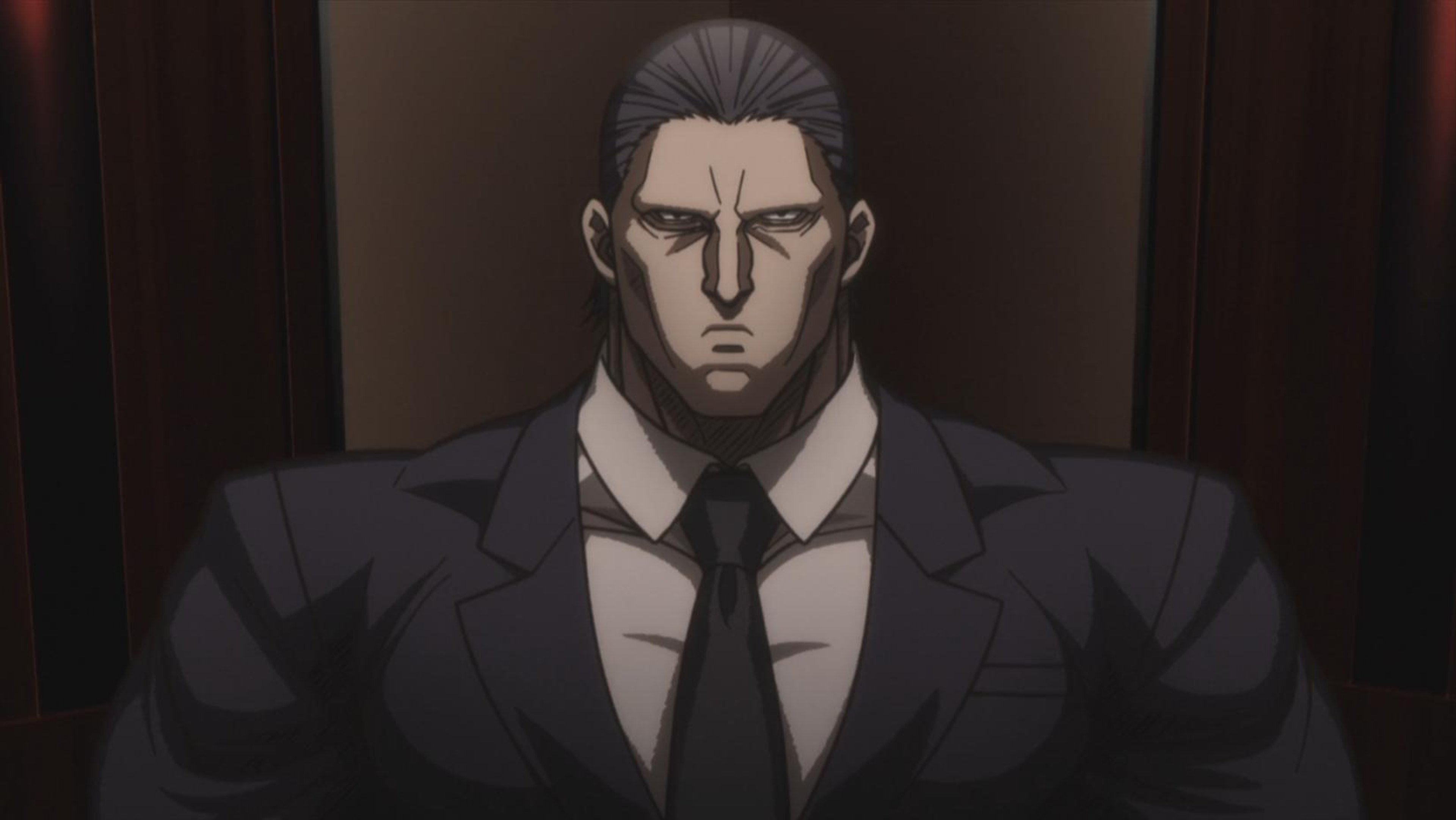 A serious-looking, muscular man in a dark suit and tie