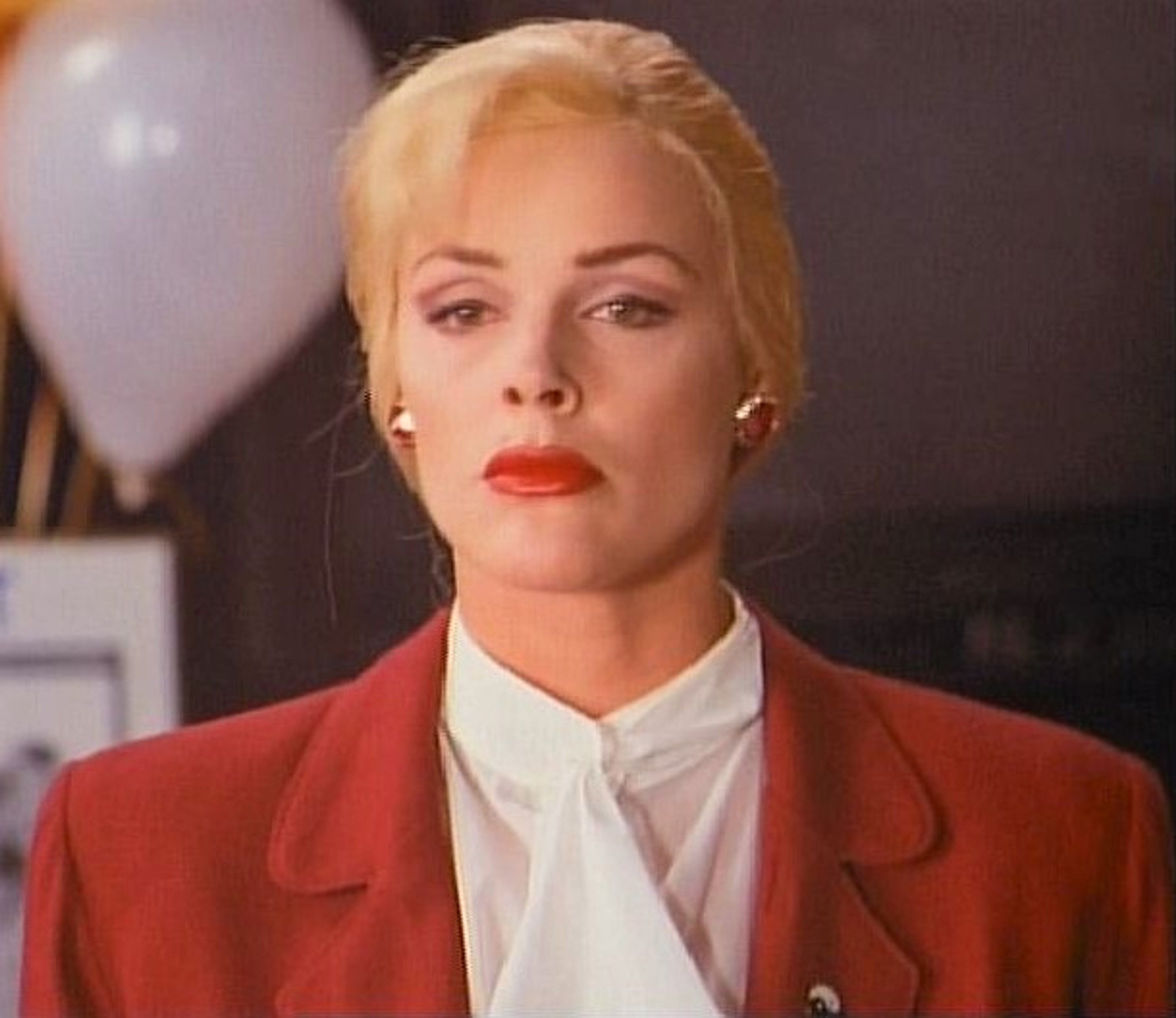 A woman in a red suit jacket with a serious expression