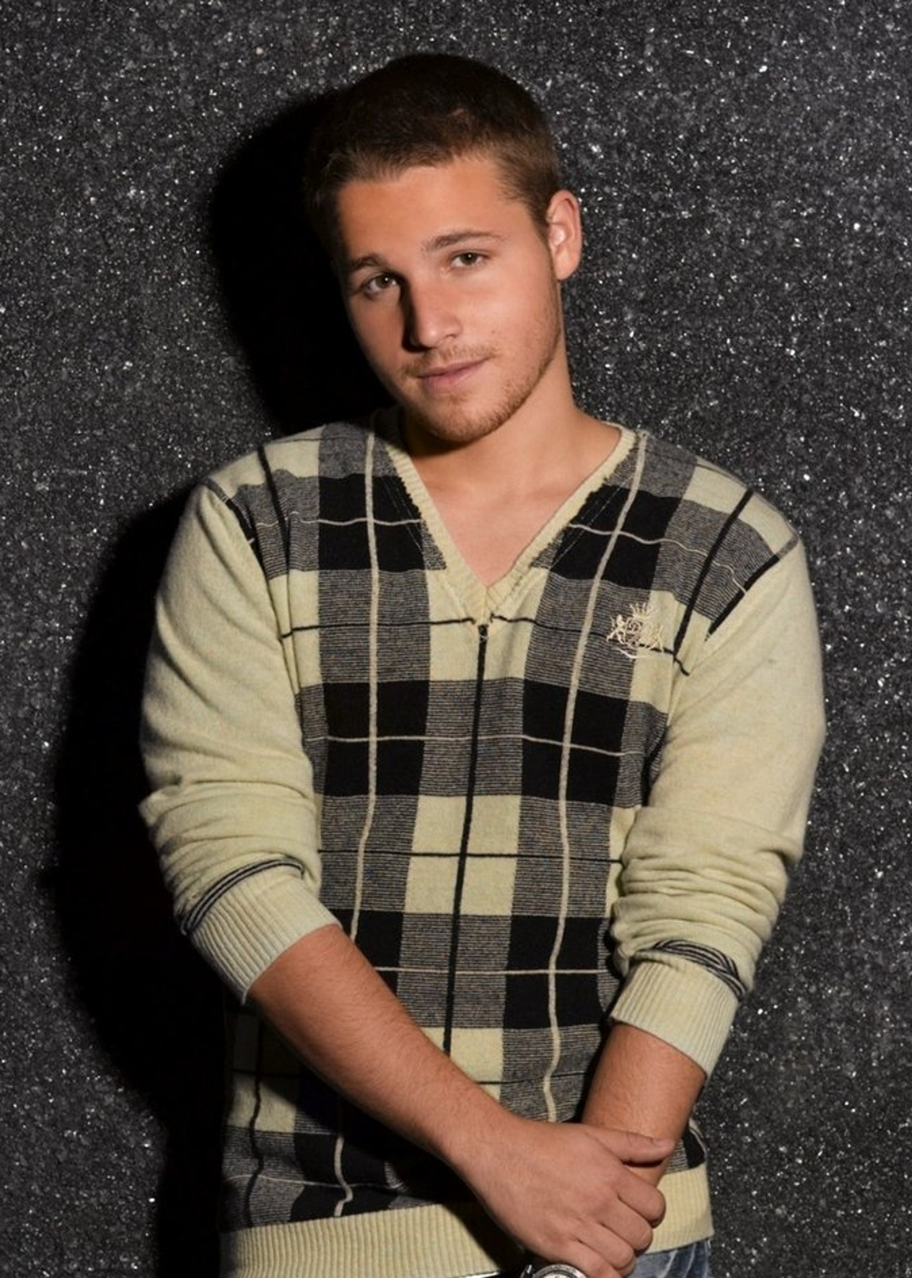 A young man with short brown hair wearing a plaid sweater