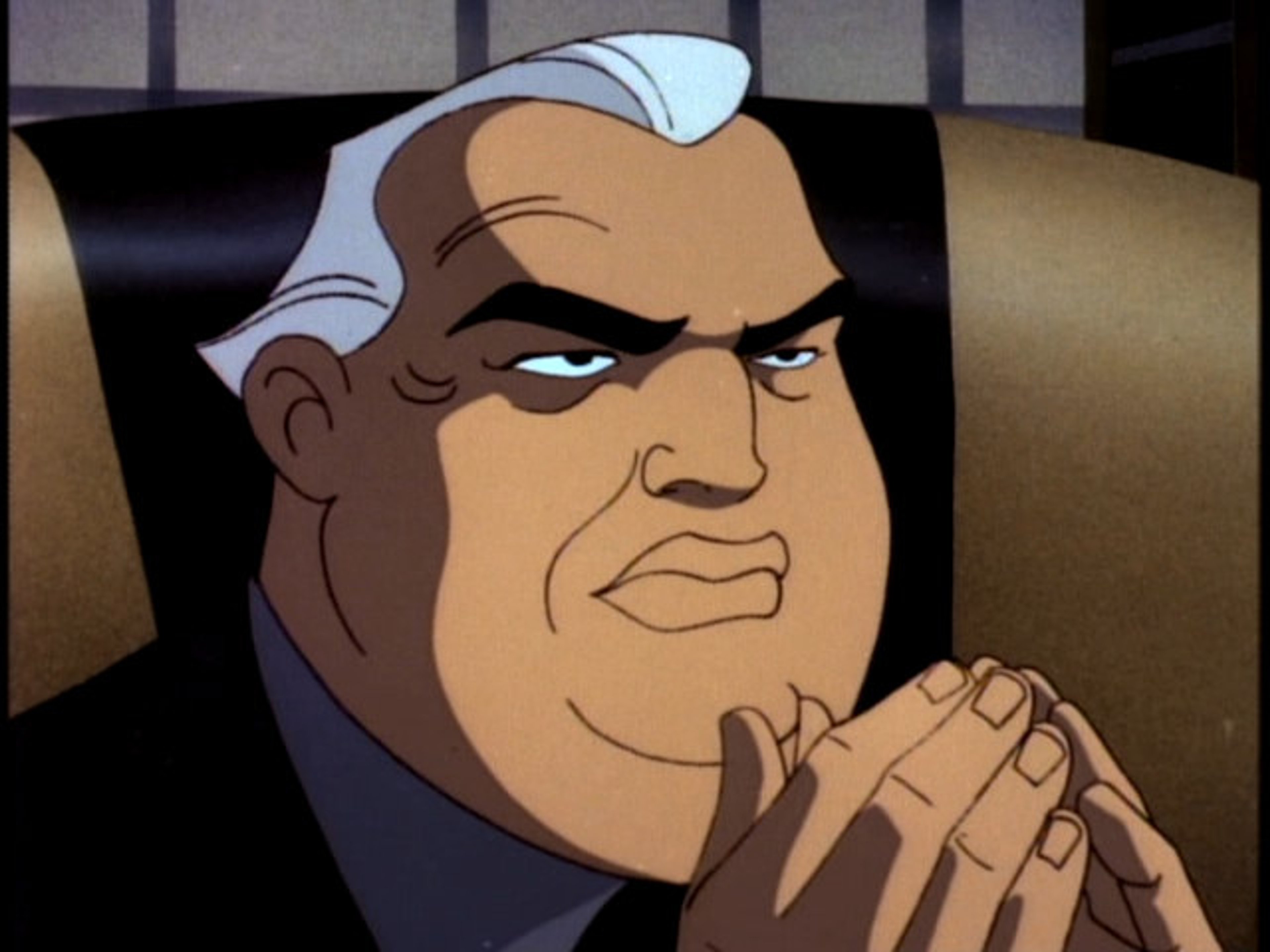 An animated, middle-aged man with a stern expression wearing a dark suit