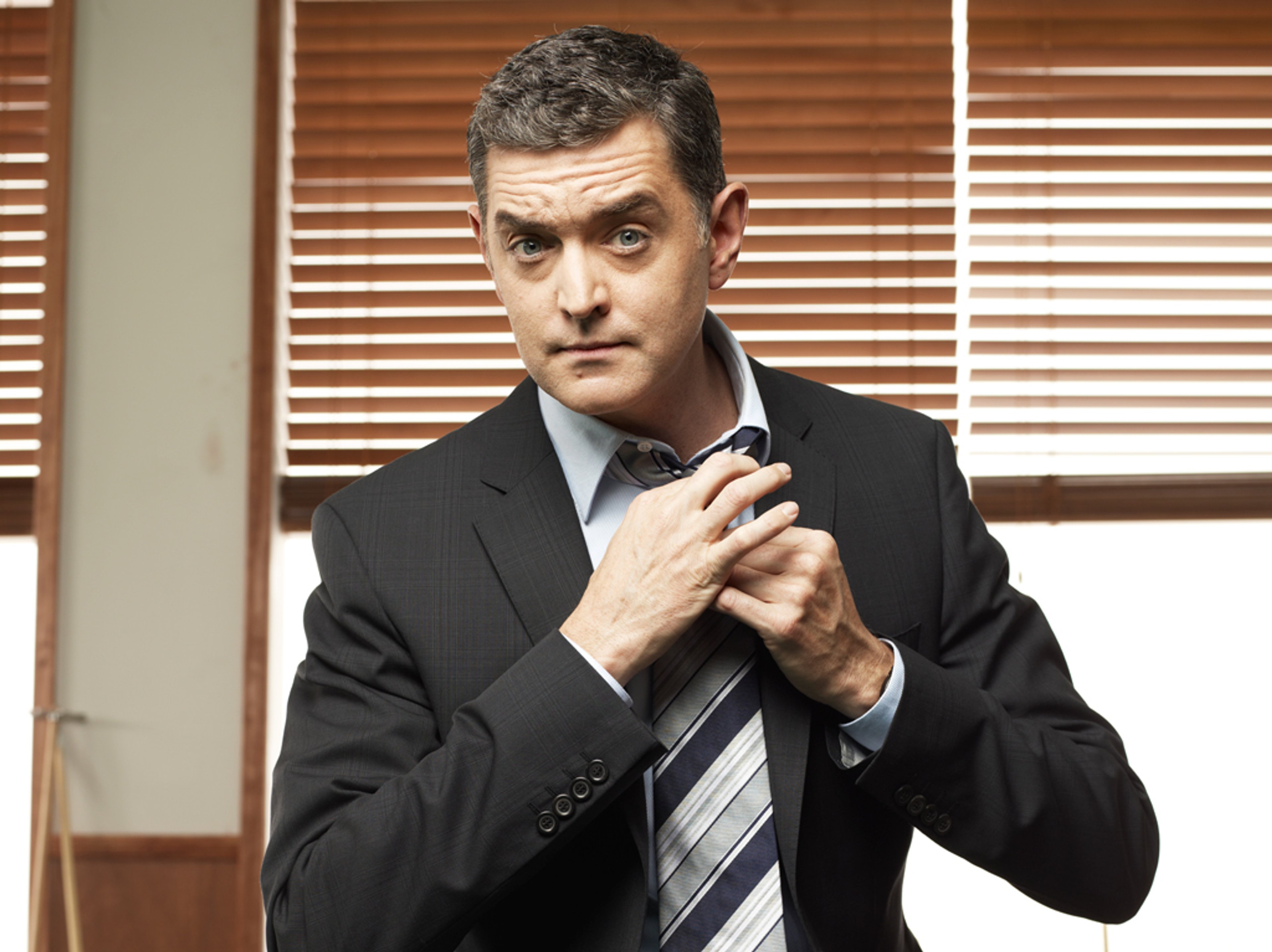 A middle-aged man in a suit and tie, with a serious expression, standing in an office or police station setting.