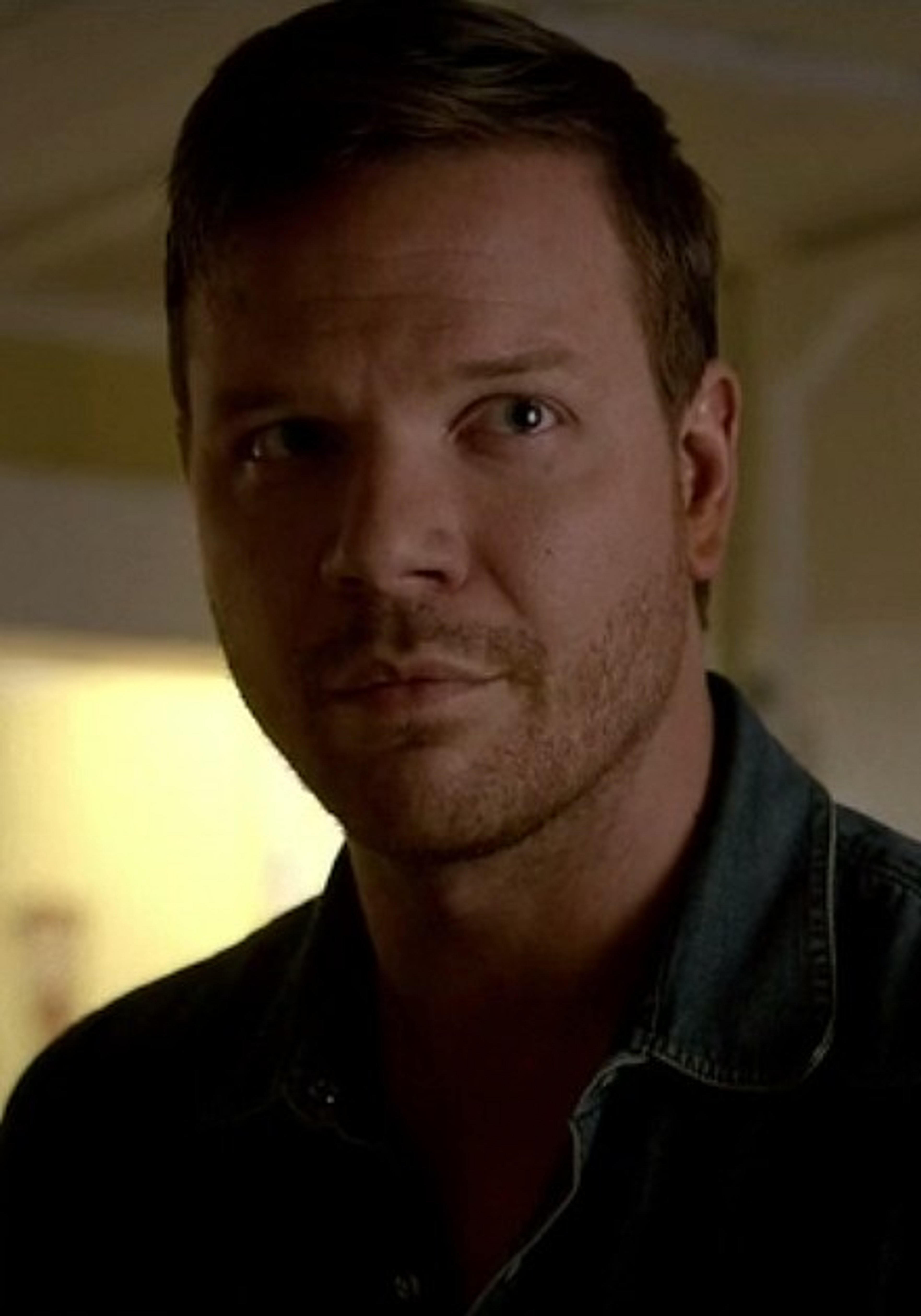 A man with short dark hair and a beard wearing a black leather jacket, with a serious expression on his face.