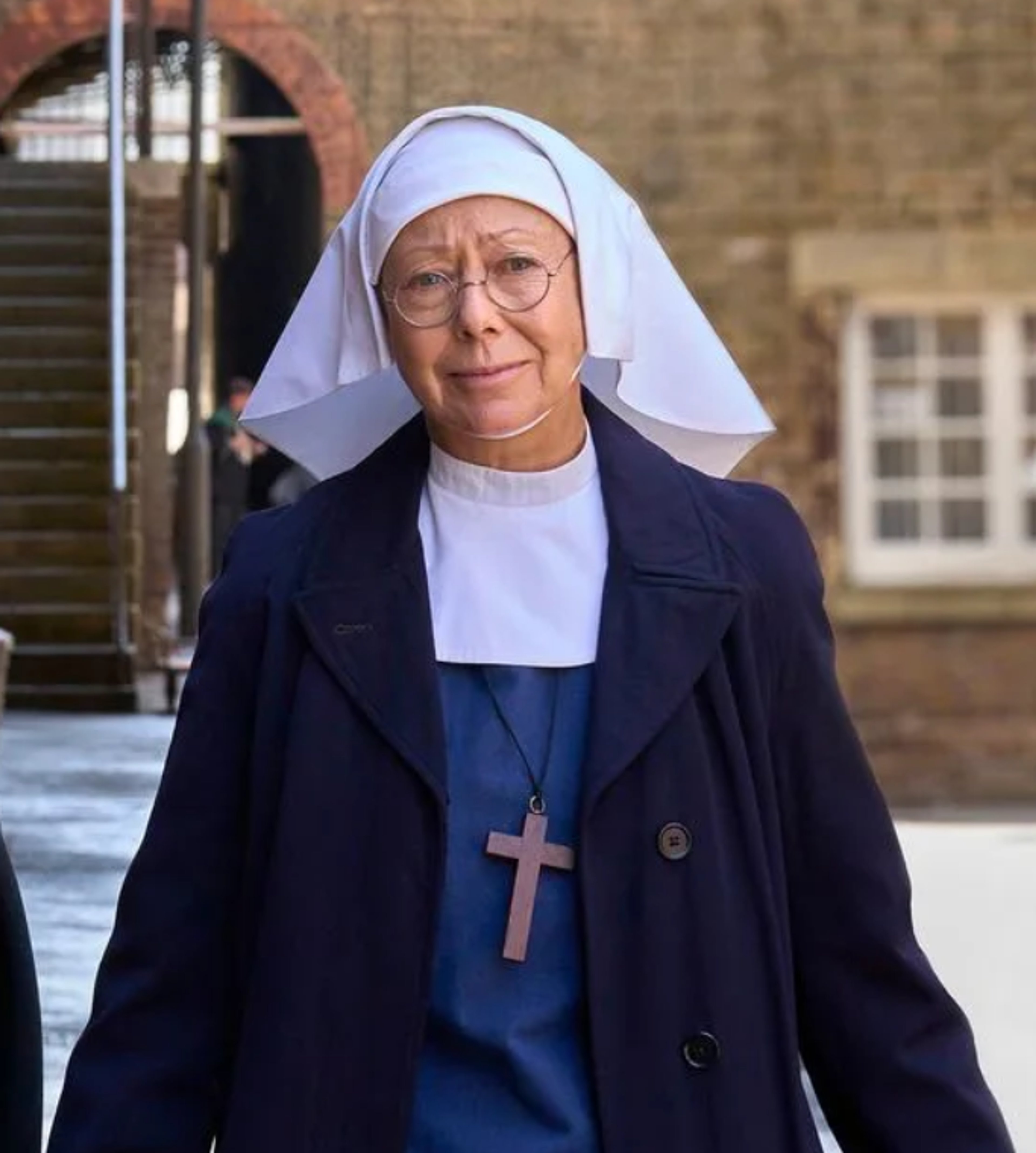 An elderly nun wearing a white veil and habit, with a kind expression on her face.