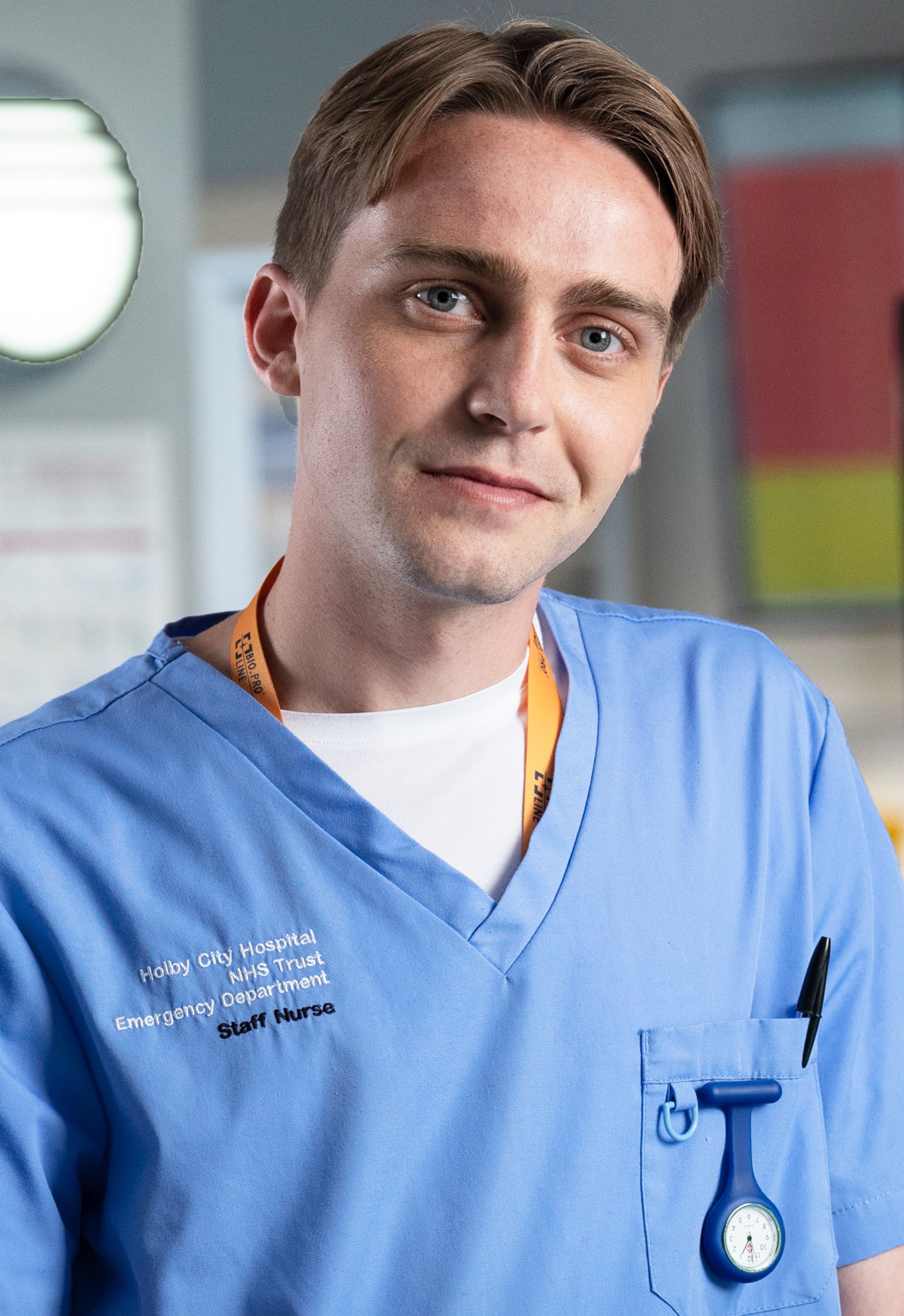 A young male nurse in blue medical scrubs standing in a hospital setting