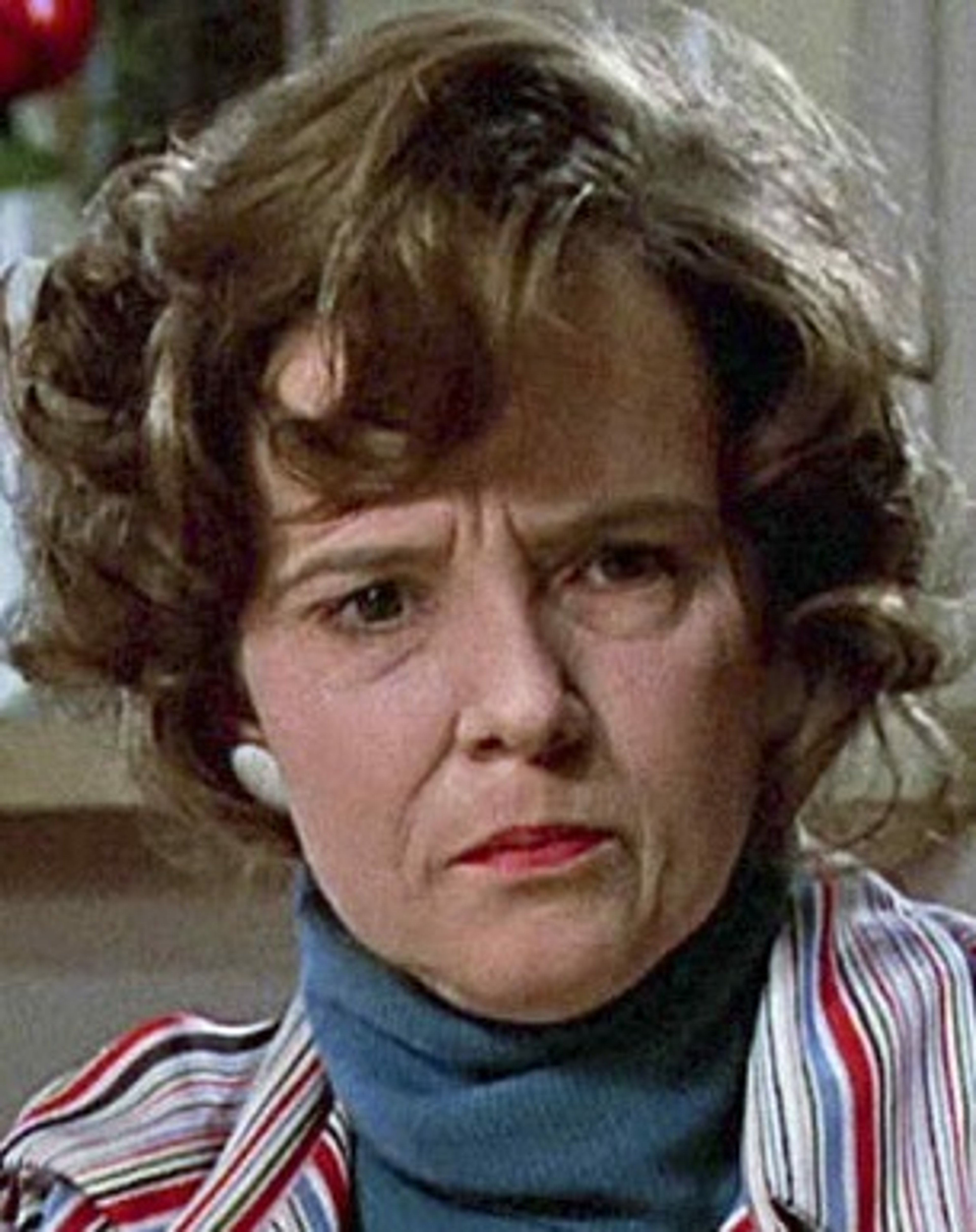A middle-aged woman with curly brown hair and a concerned expression