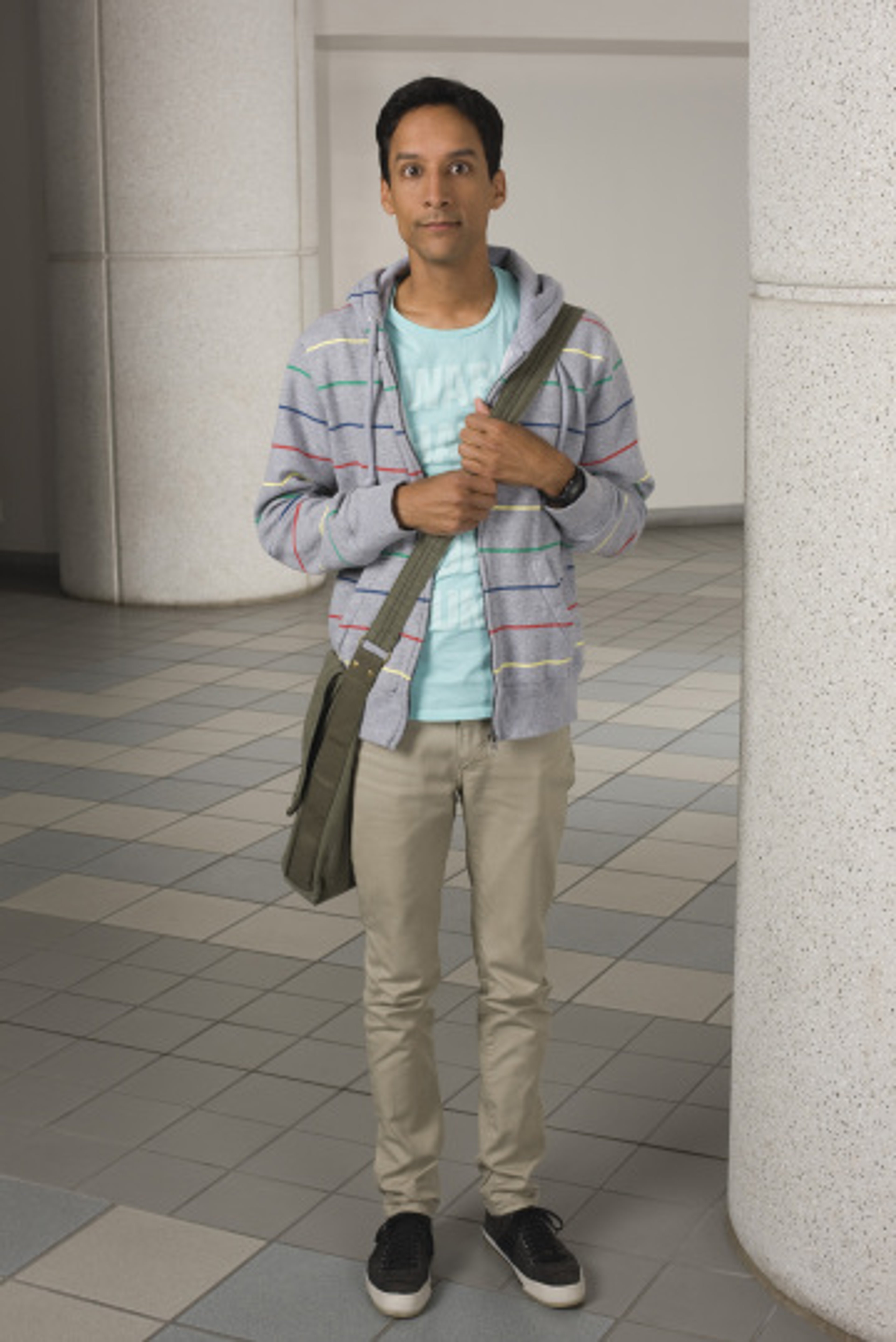 A young man with dark hair wearing a plaid shirt, khaki pants, and sneakers