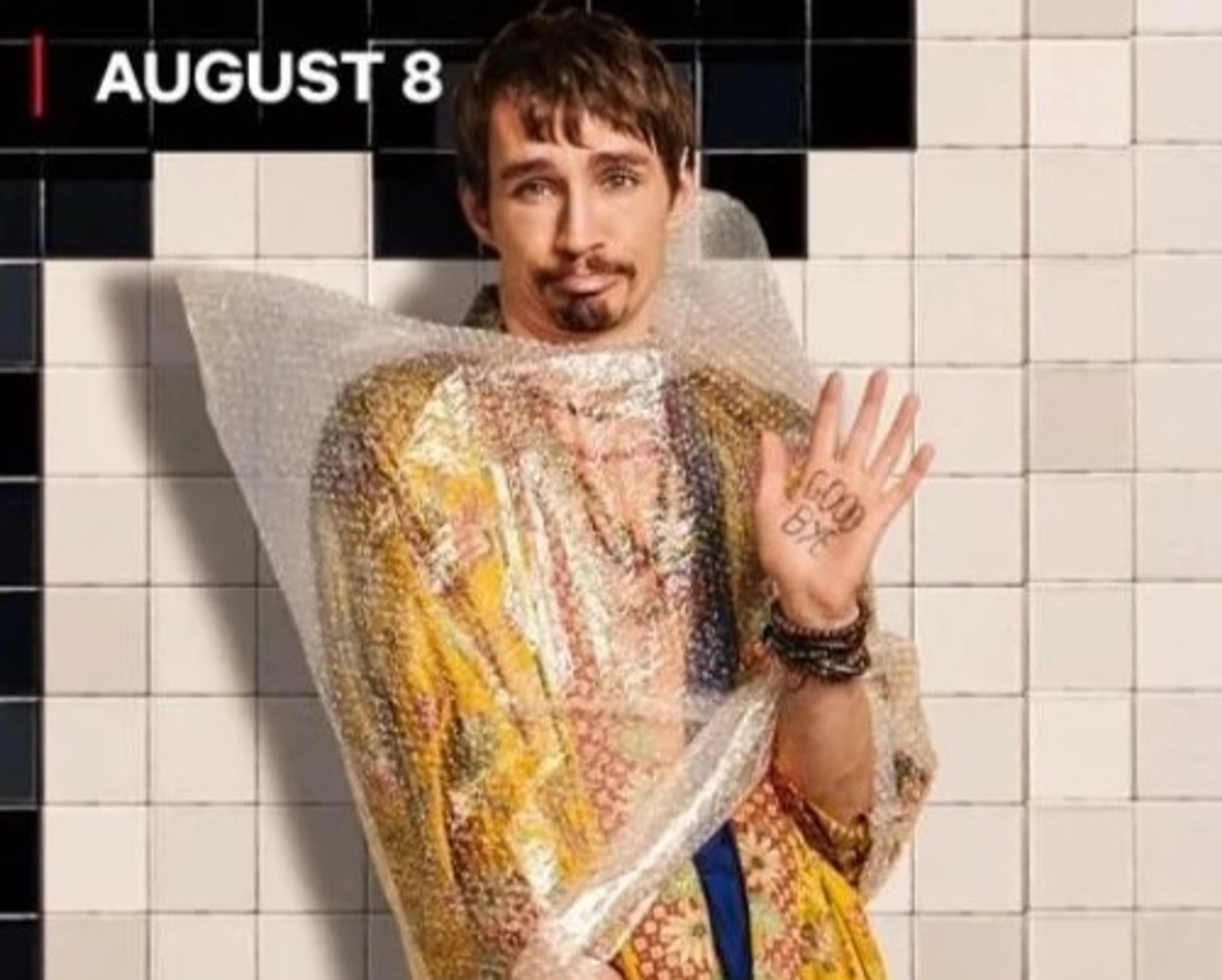 A man with long, curly brown hair and facial hair wearing a colorful, patterned shirt