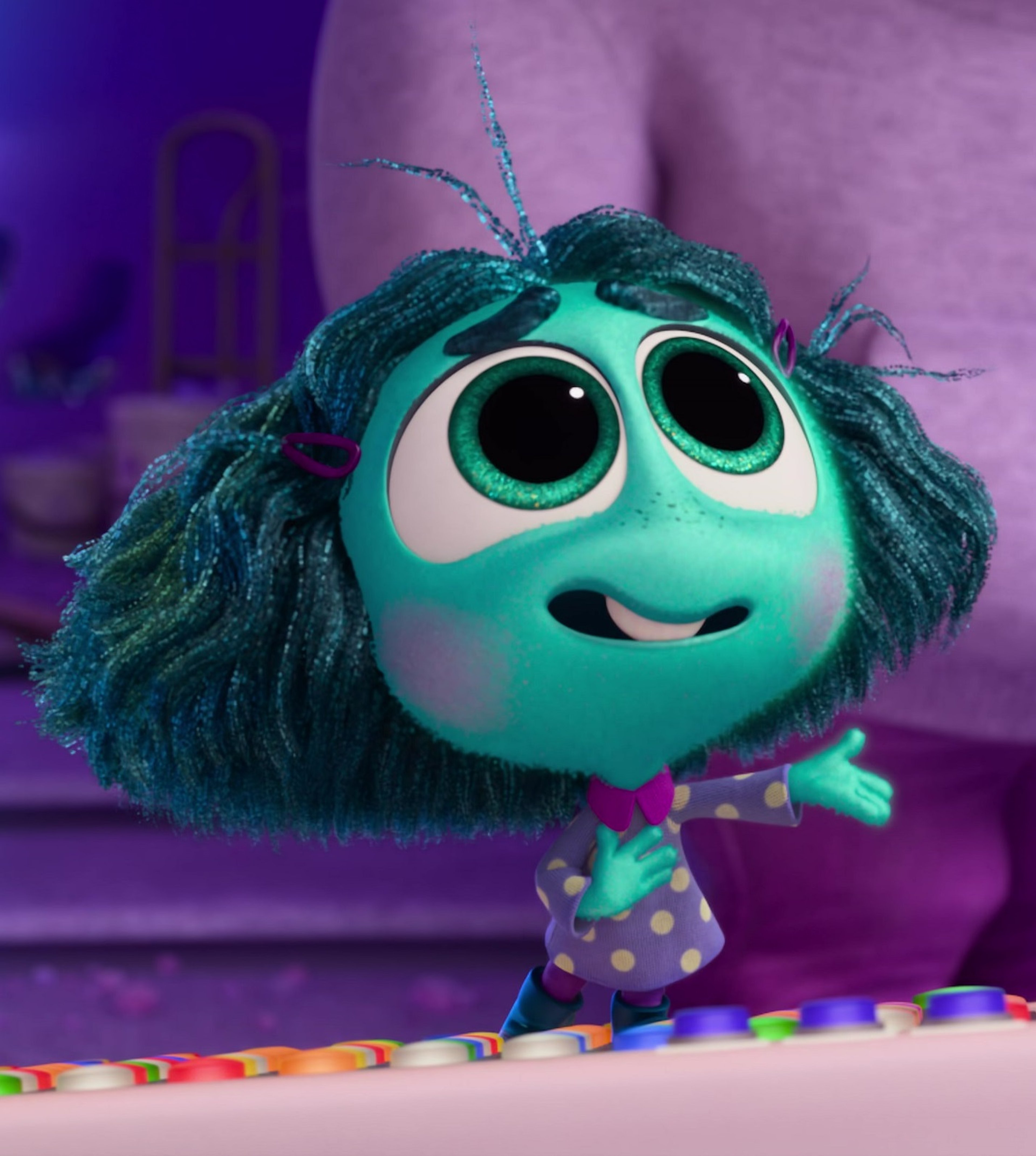 A small, aquamarine-colored character with large eyes and green hair, wearing a polka dot dress.