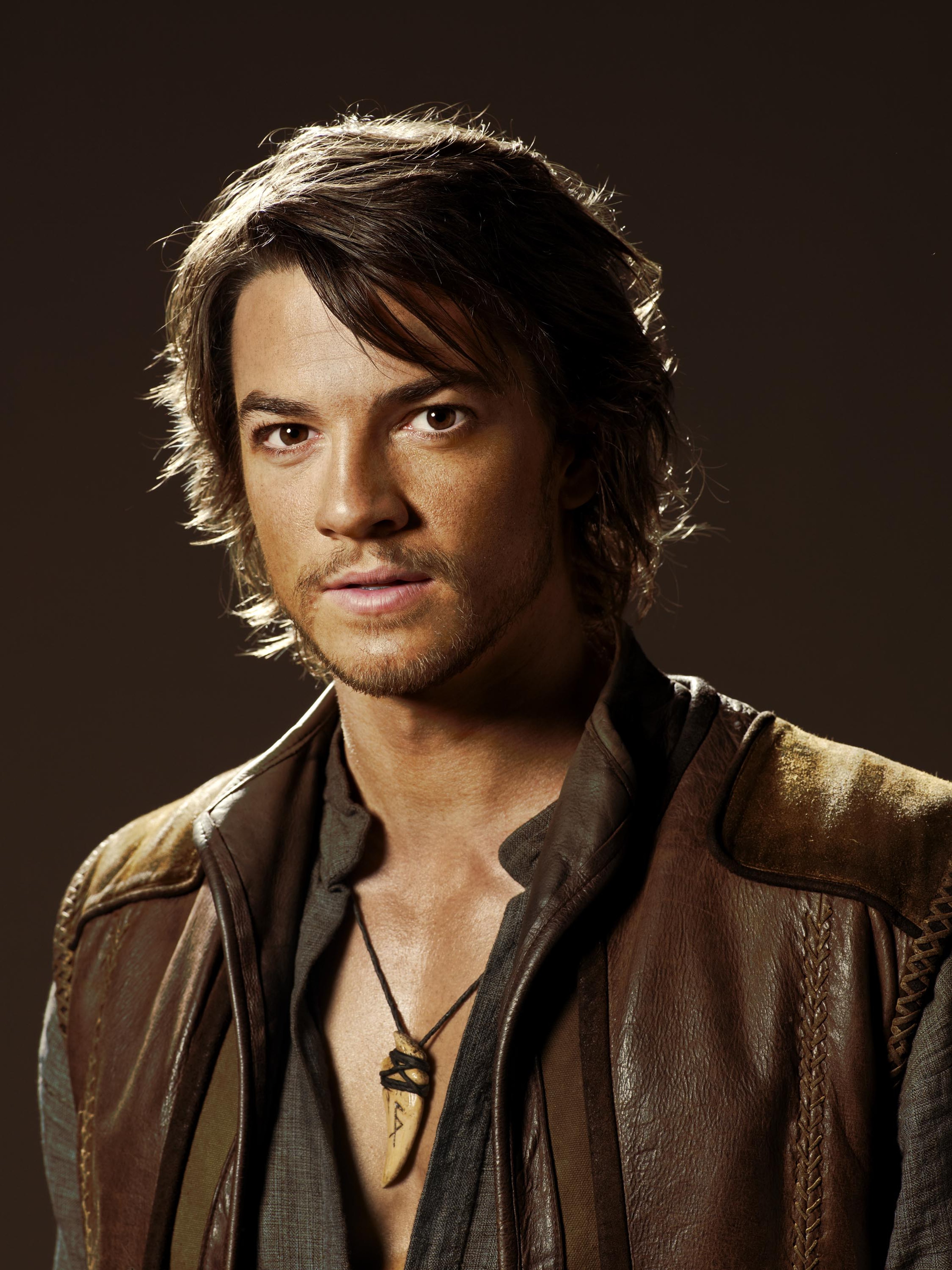 A man with long dark hair and a rugged appearance wearing a brown leather jacket