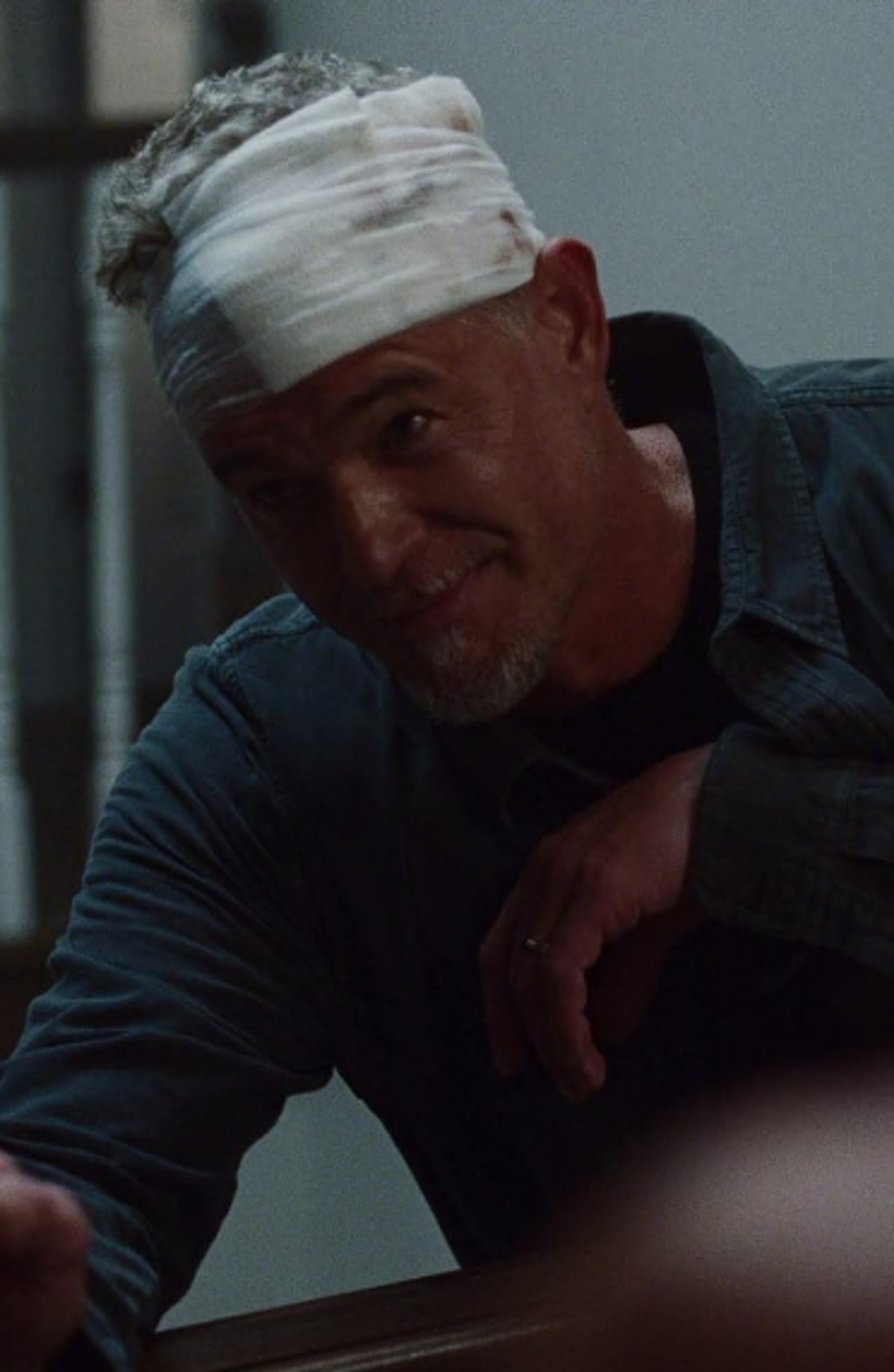 A middle-aged man with short gray hair and a beard, wearing a blue shirt and looking serious.