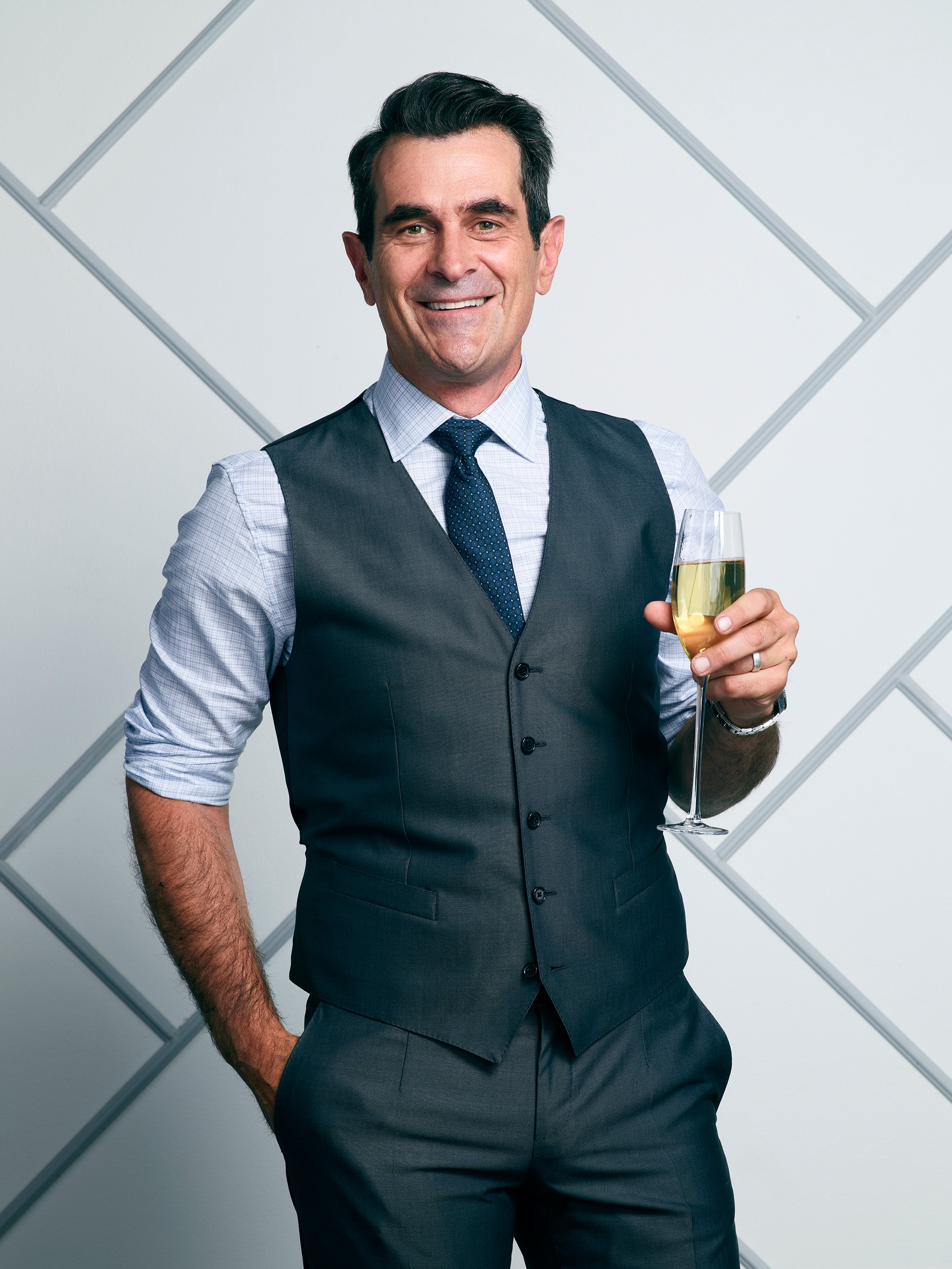 A well-dressed middle-aged man holding a glass of alcohol and smiling