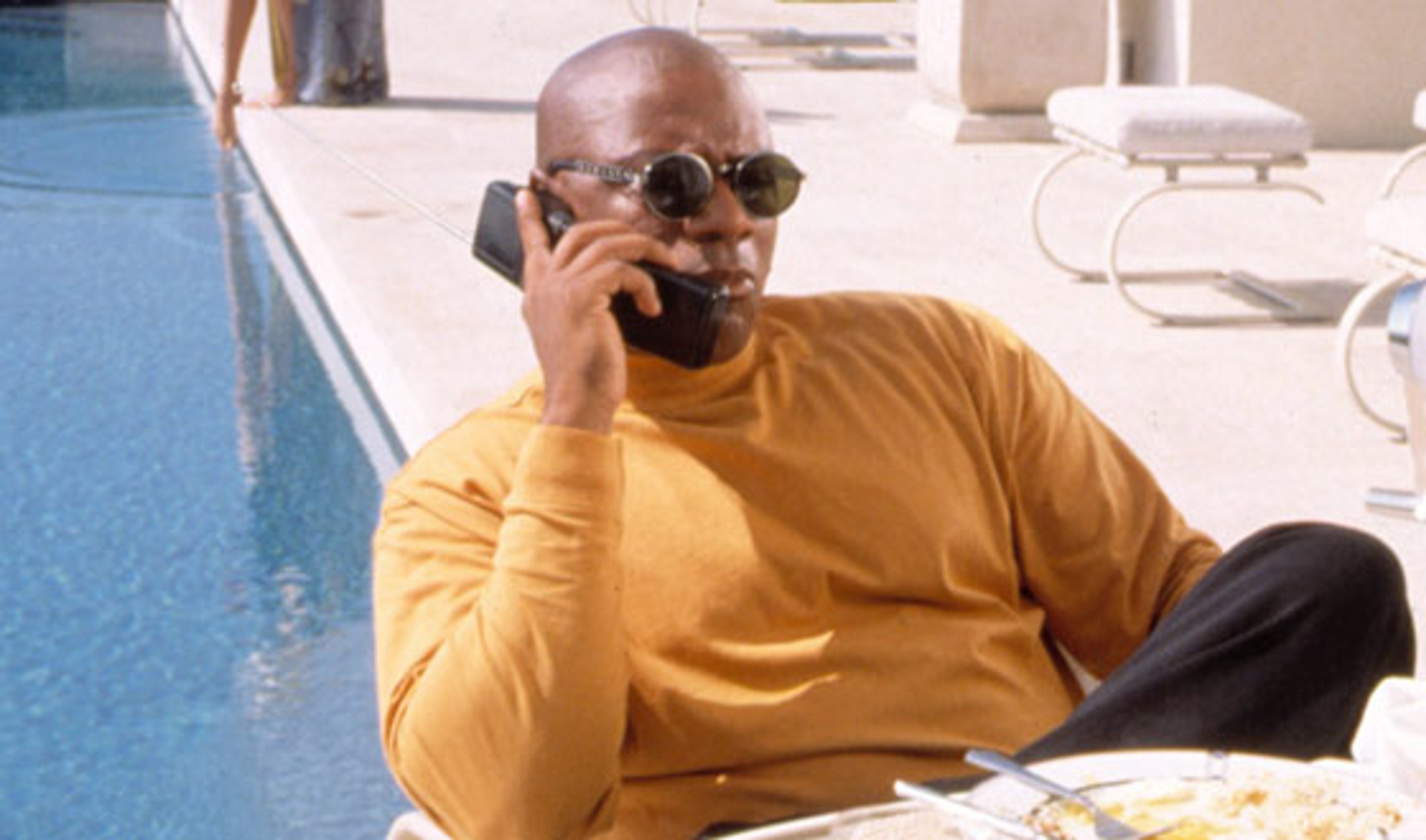 A bald, African-American man sitting by a pool