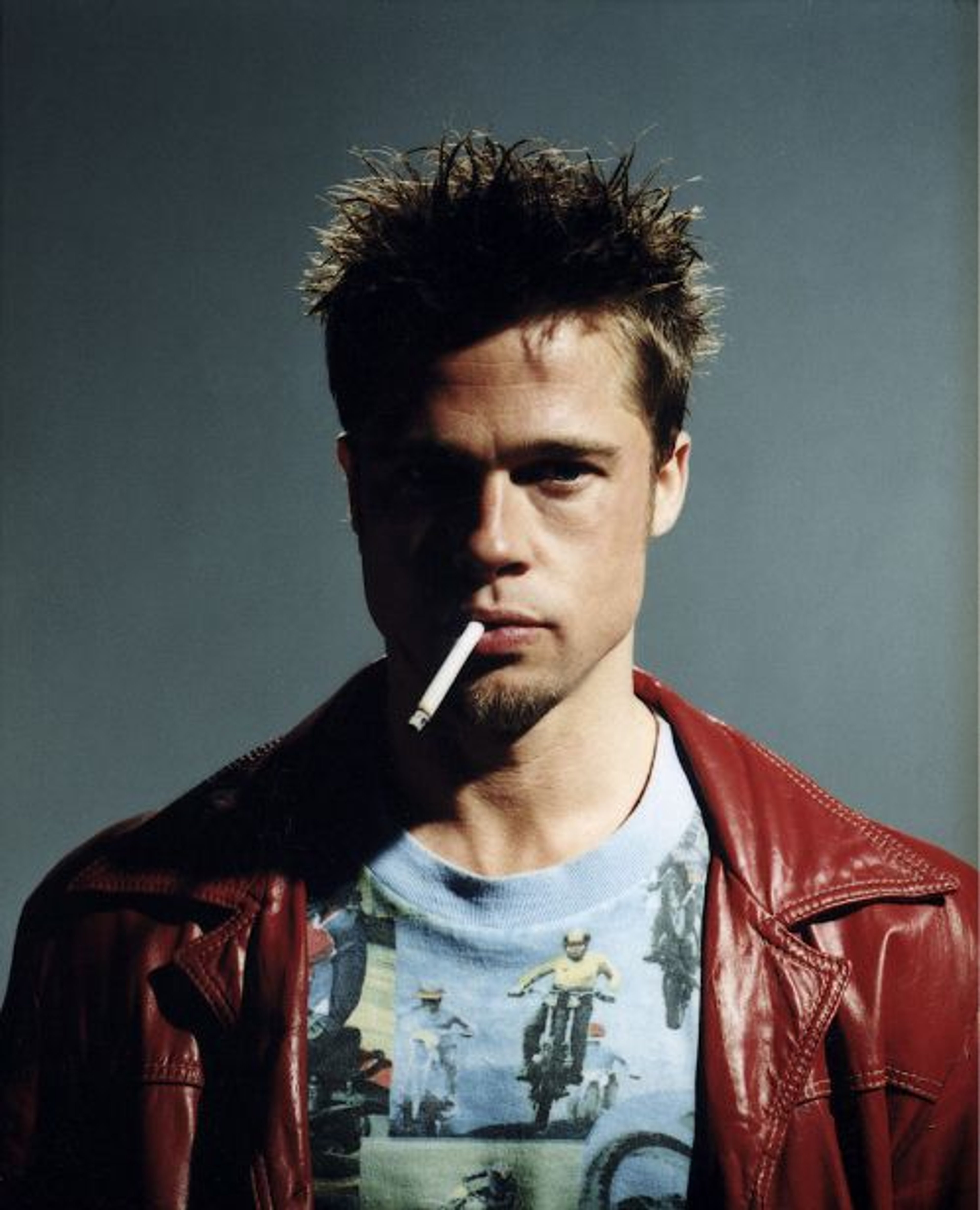 A man with short, dark hair wearing a red leather jacket and smoking a cigarette