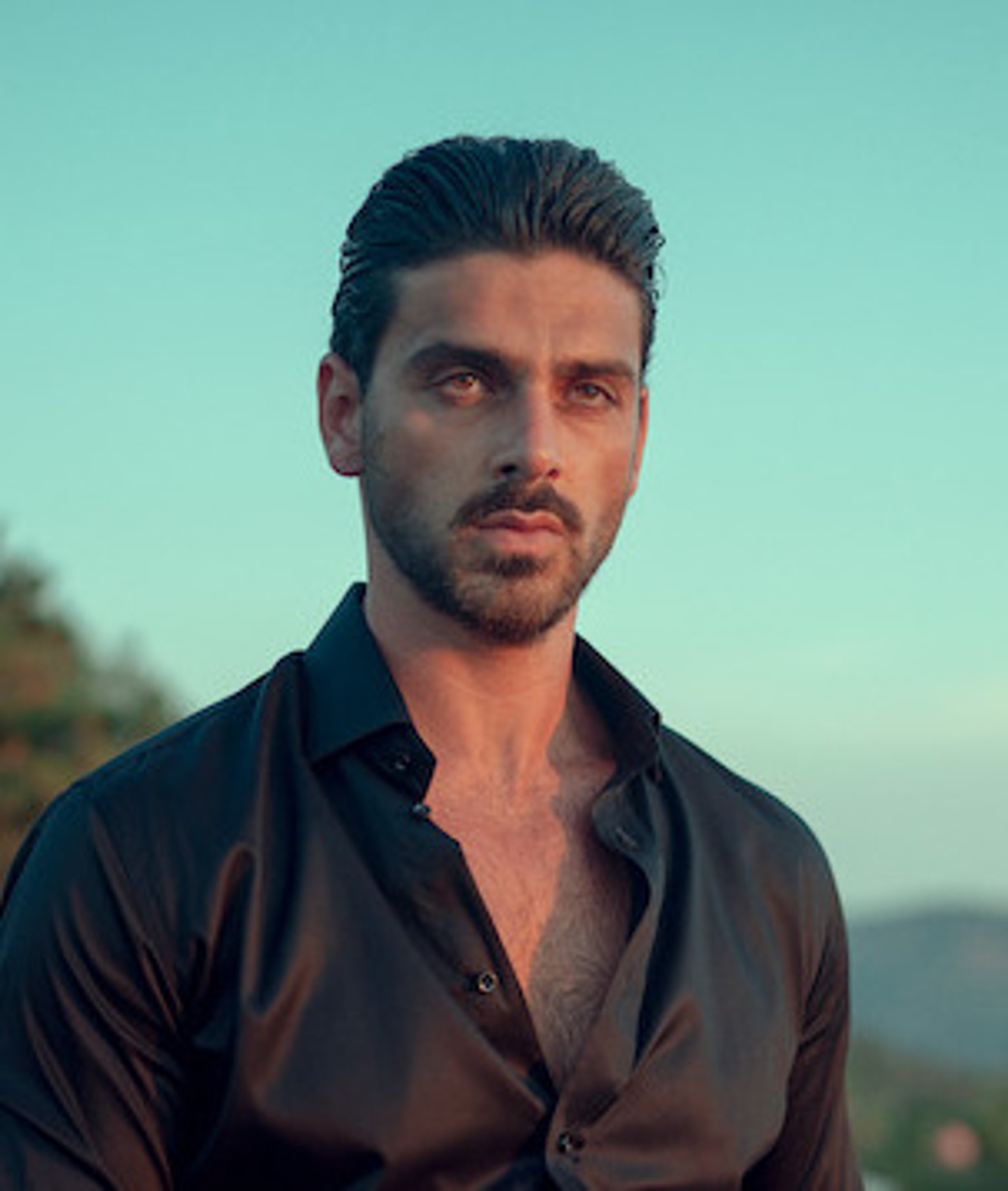 A man with dark hair and a beard wearing a black shirt, looking serious and intense.