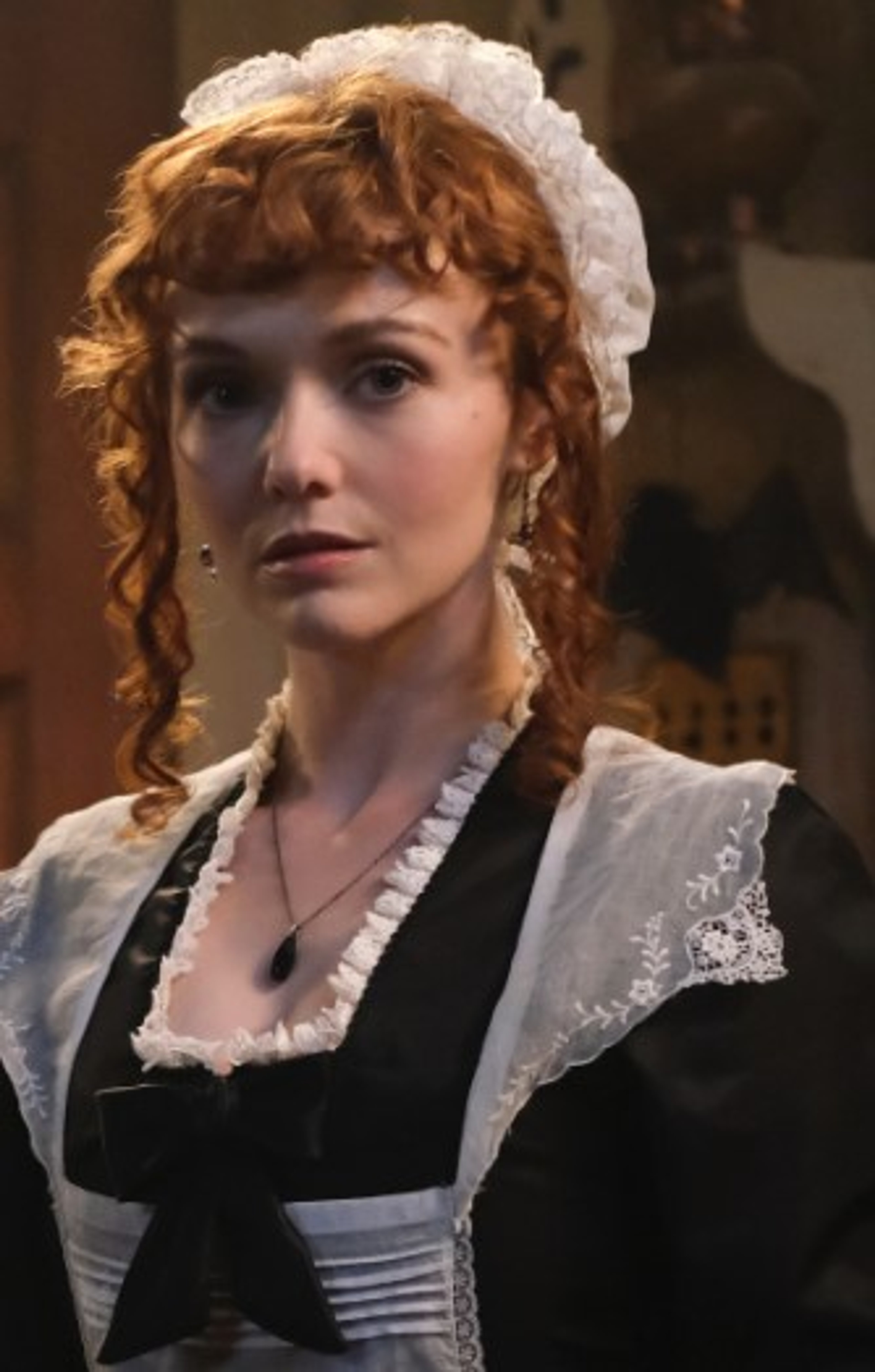 A young woman with red curly hair wearing a white blouse and black bodice in a historical setting