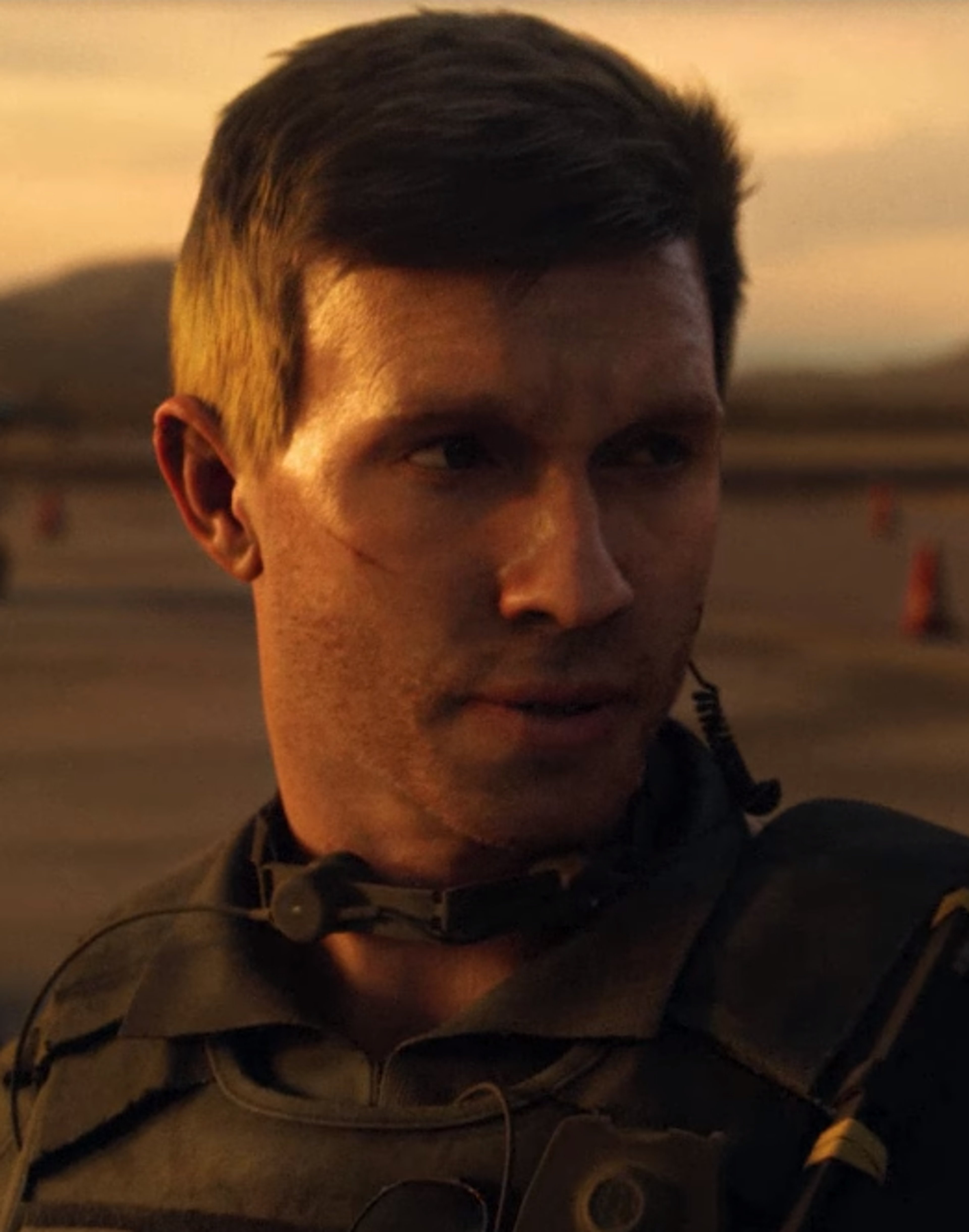 A man with short dark hair wearing a military jacket in a desert setting