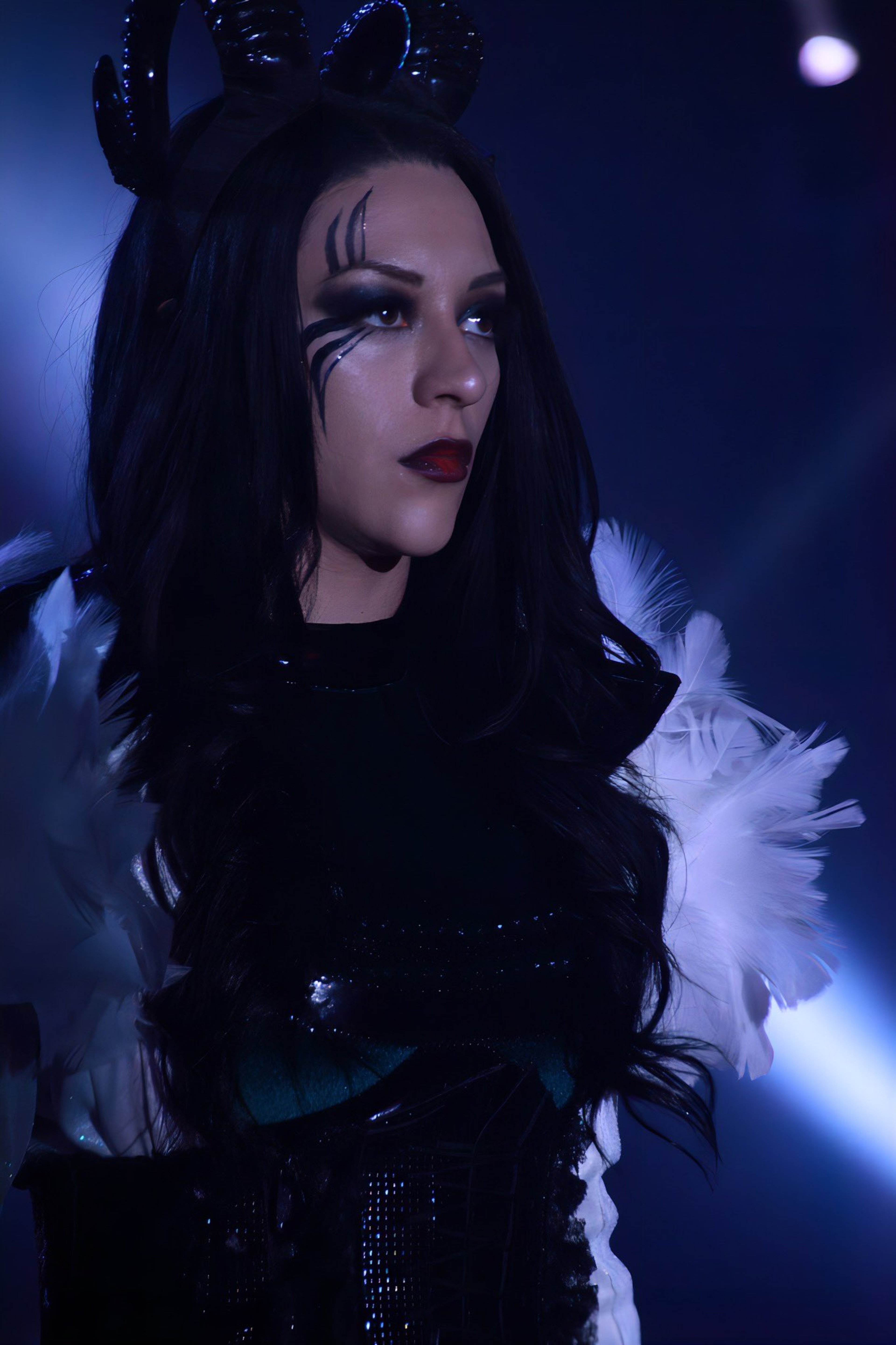 A woman with dark hair and intense expression wearing a black feathered outfit