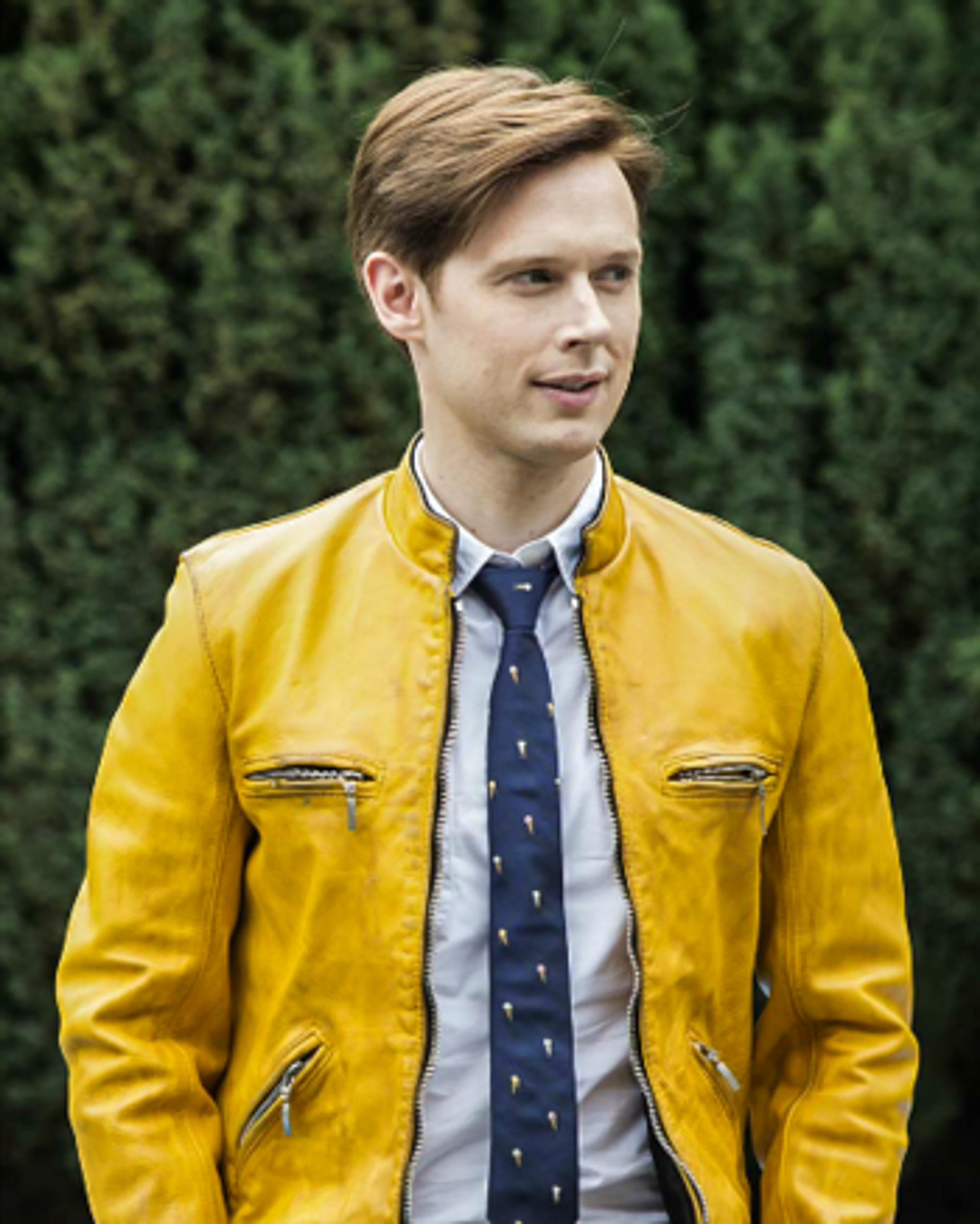 A young man with blonde hair wearing a yellow jacket and blue tie