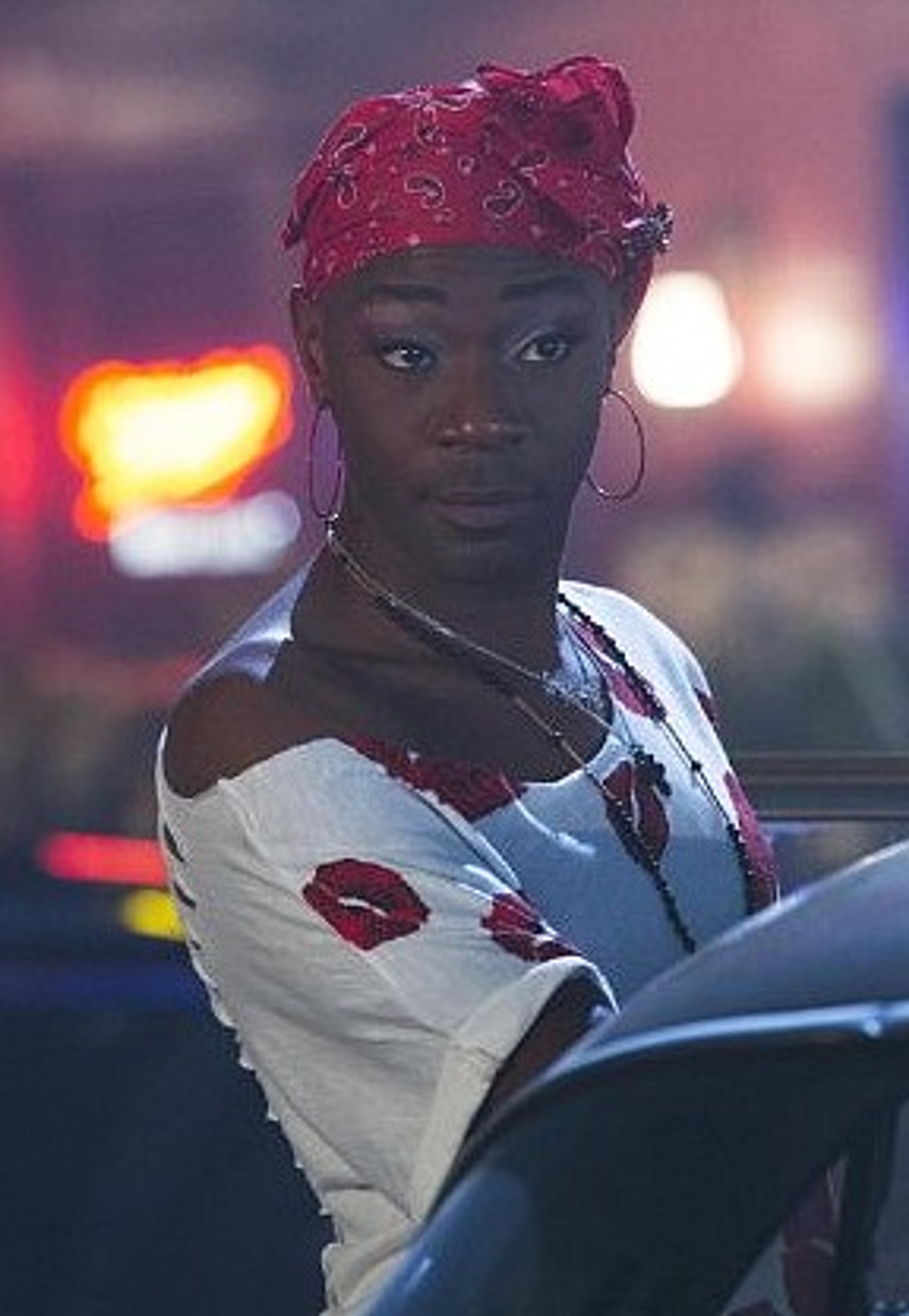 A Black man with a red bandana on his head, wearing a white shirt, with a serious expression on his face.