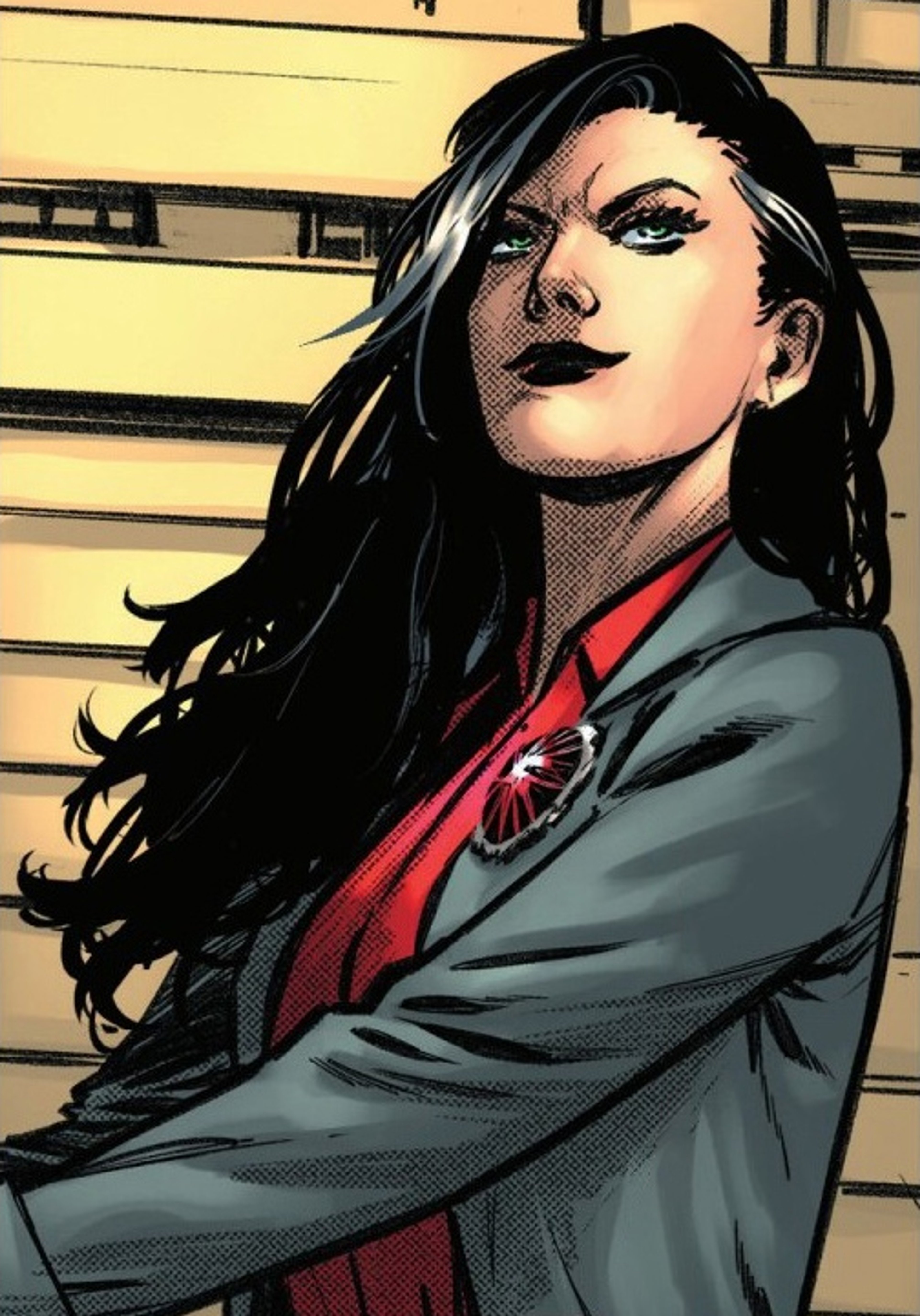A woman with dark hair wearing a gray suit jacket and red shirt, standing with her arms crossed and a serious expression.