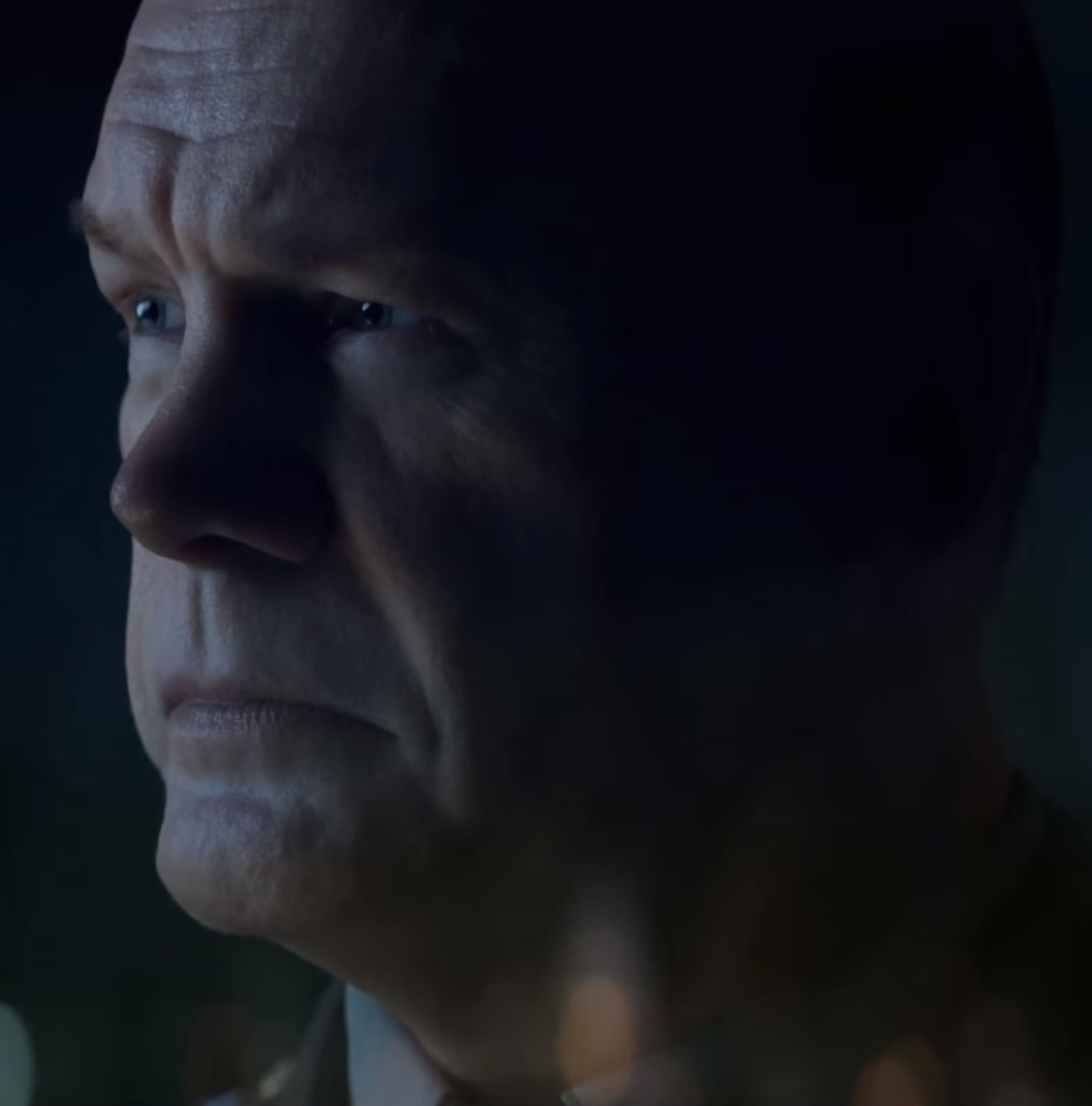 A close-up portrait of a serious-looking middle-aged man in a dark setting