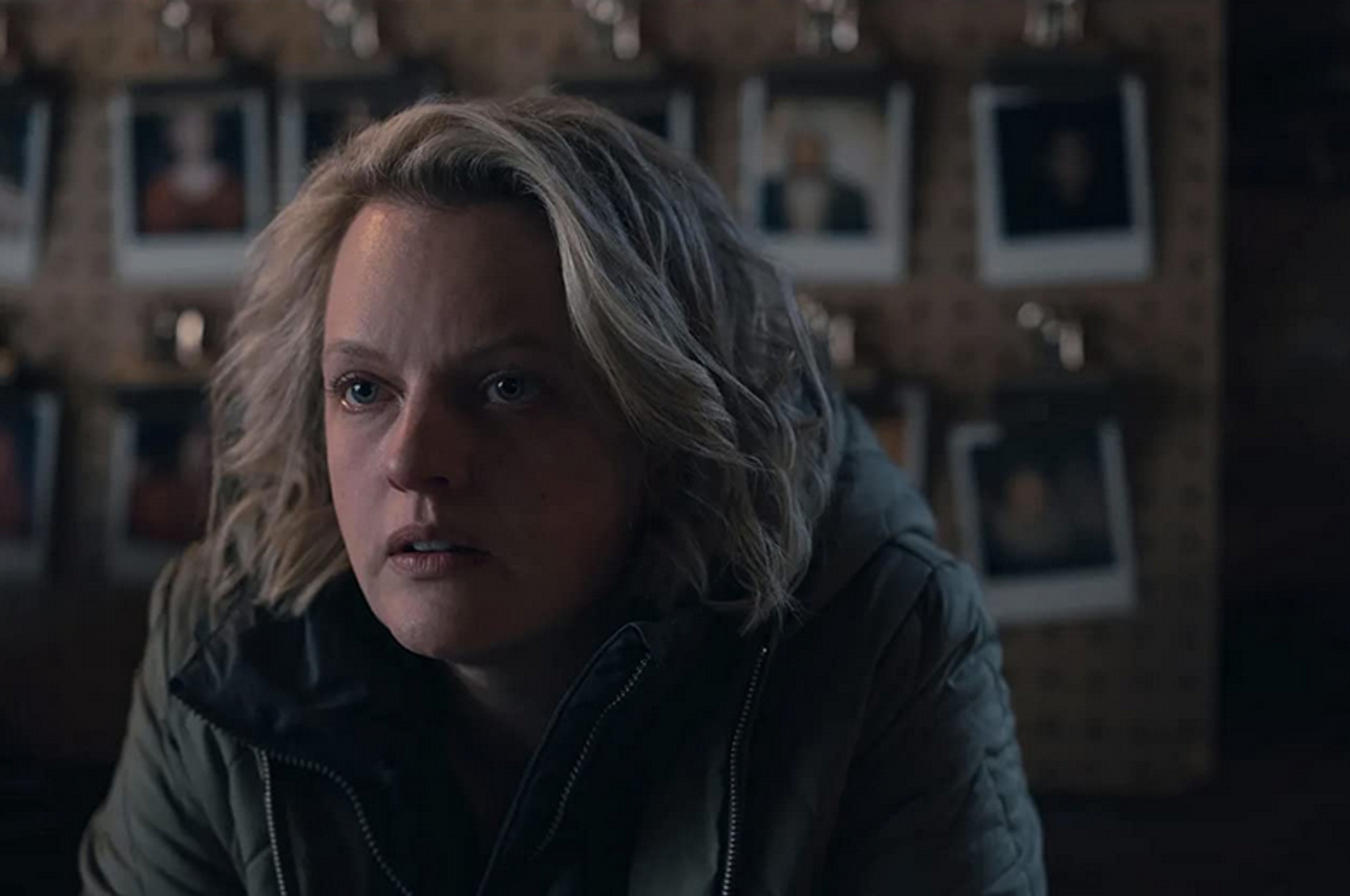 A woman with blonde hair wearing a dark jacket in a dimly lit room