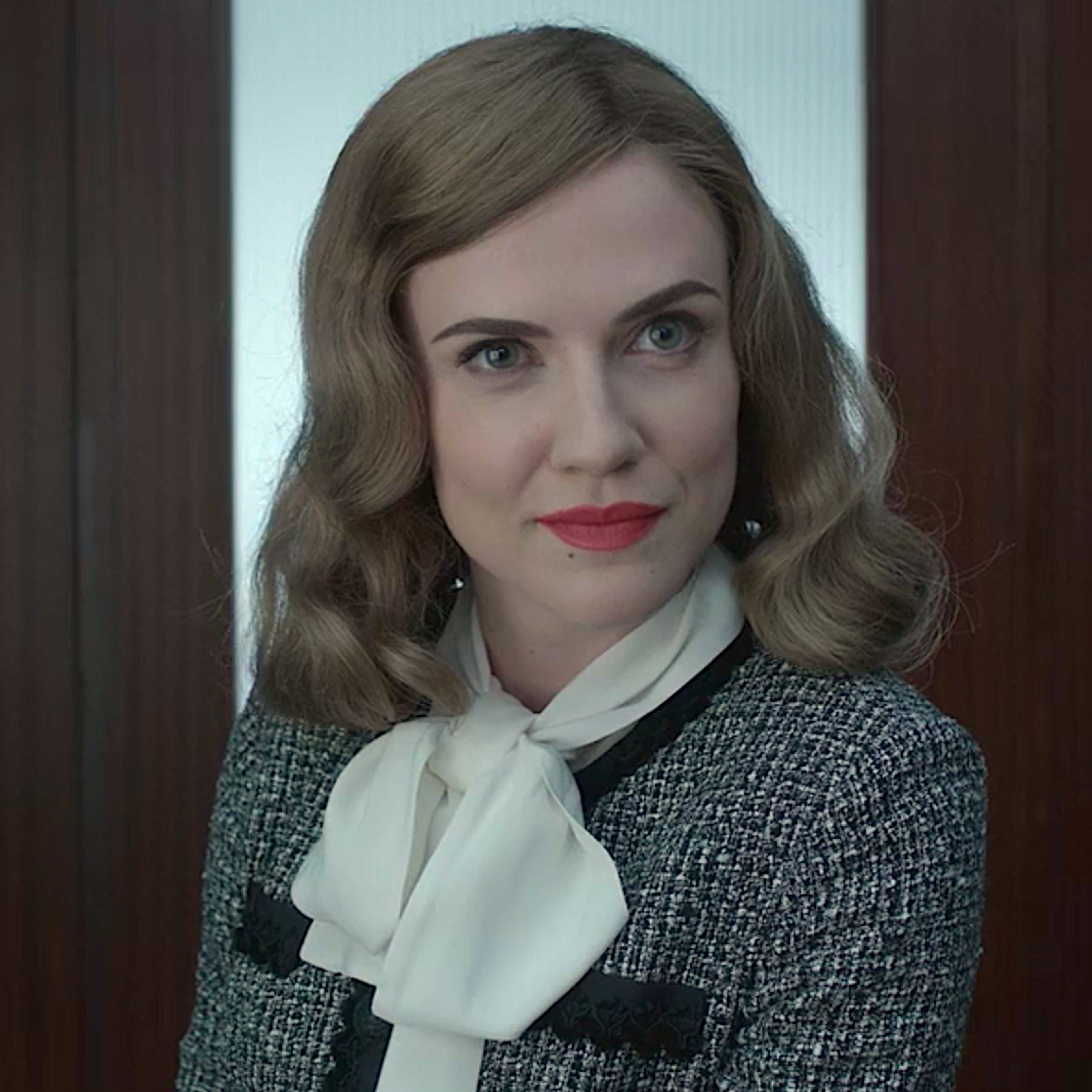 A woman with blonde hair and gray eyes wearing a black and white tweed jacket