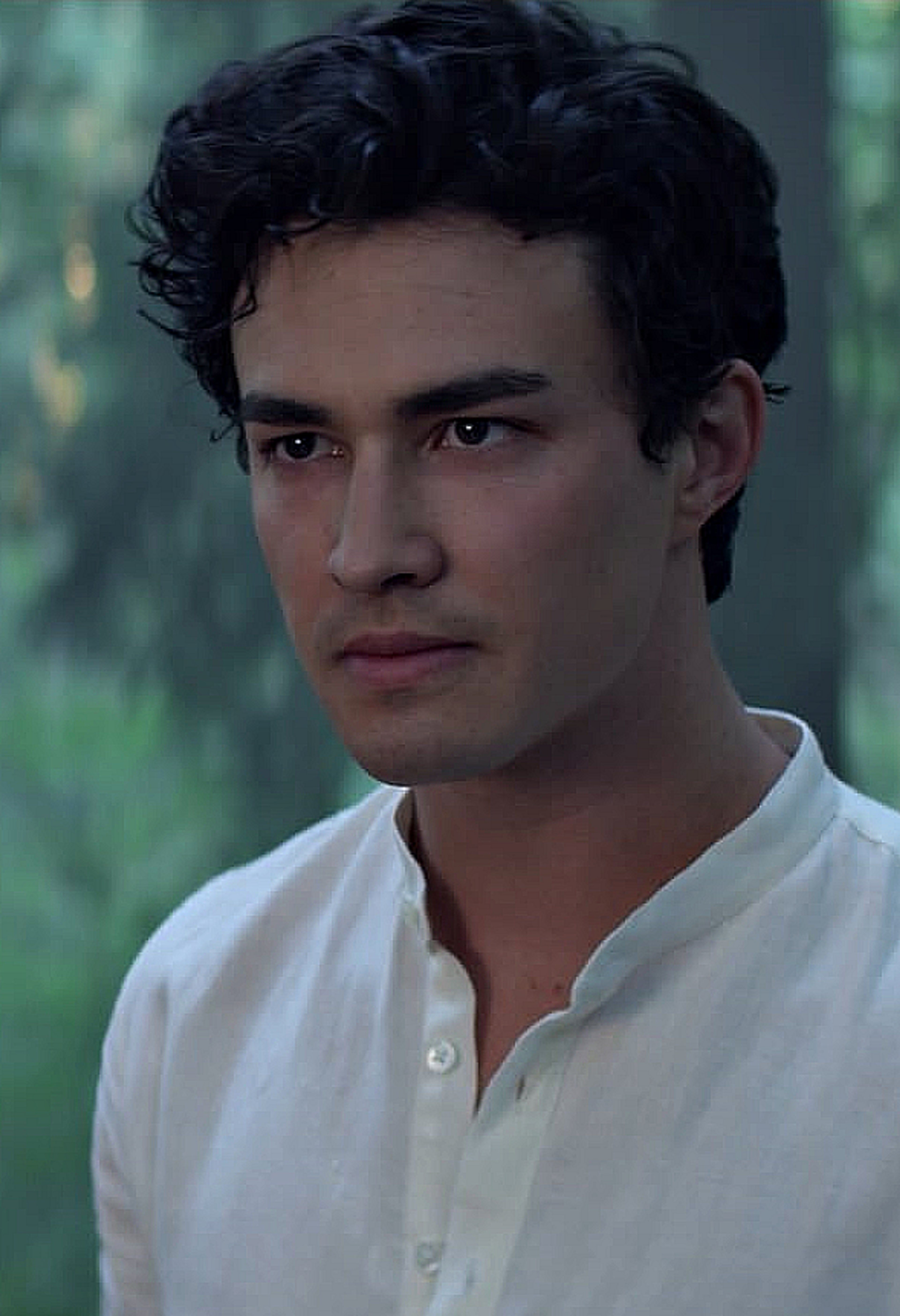 A young, handsome man with dark curly hair wearing a white shirt in an outdoor setting