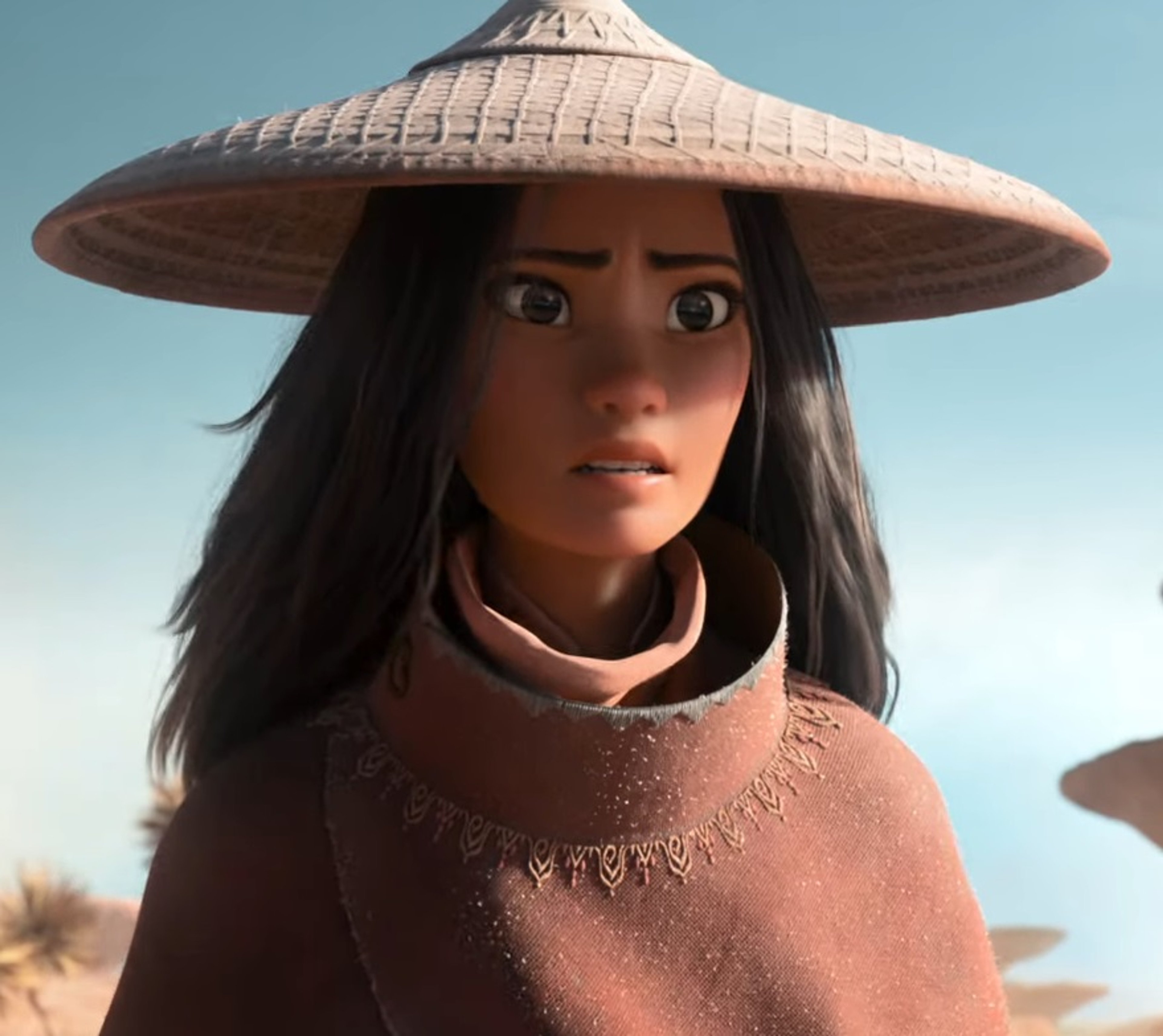 A young woman with dark hair wearing a pink scarf and conical hat in a desert setting.