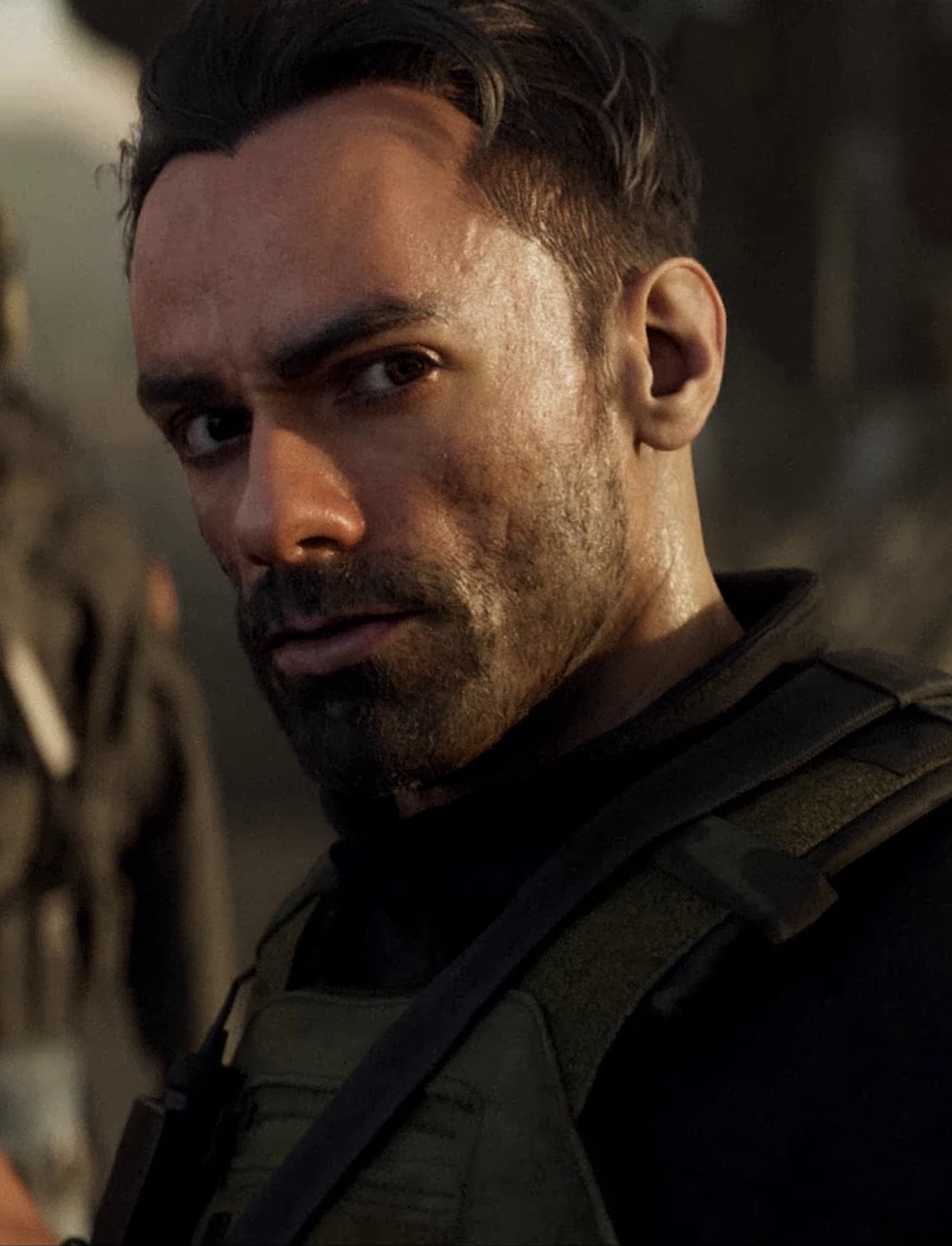 A man with a rugged, military-style appearance in a tactical vest