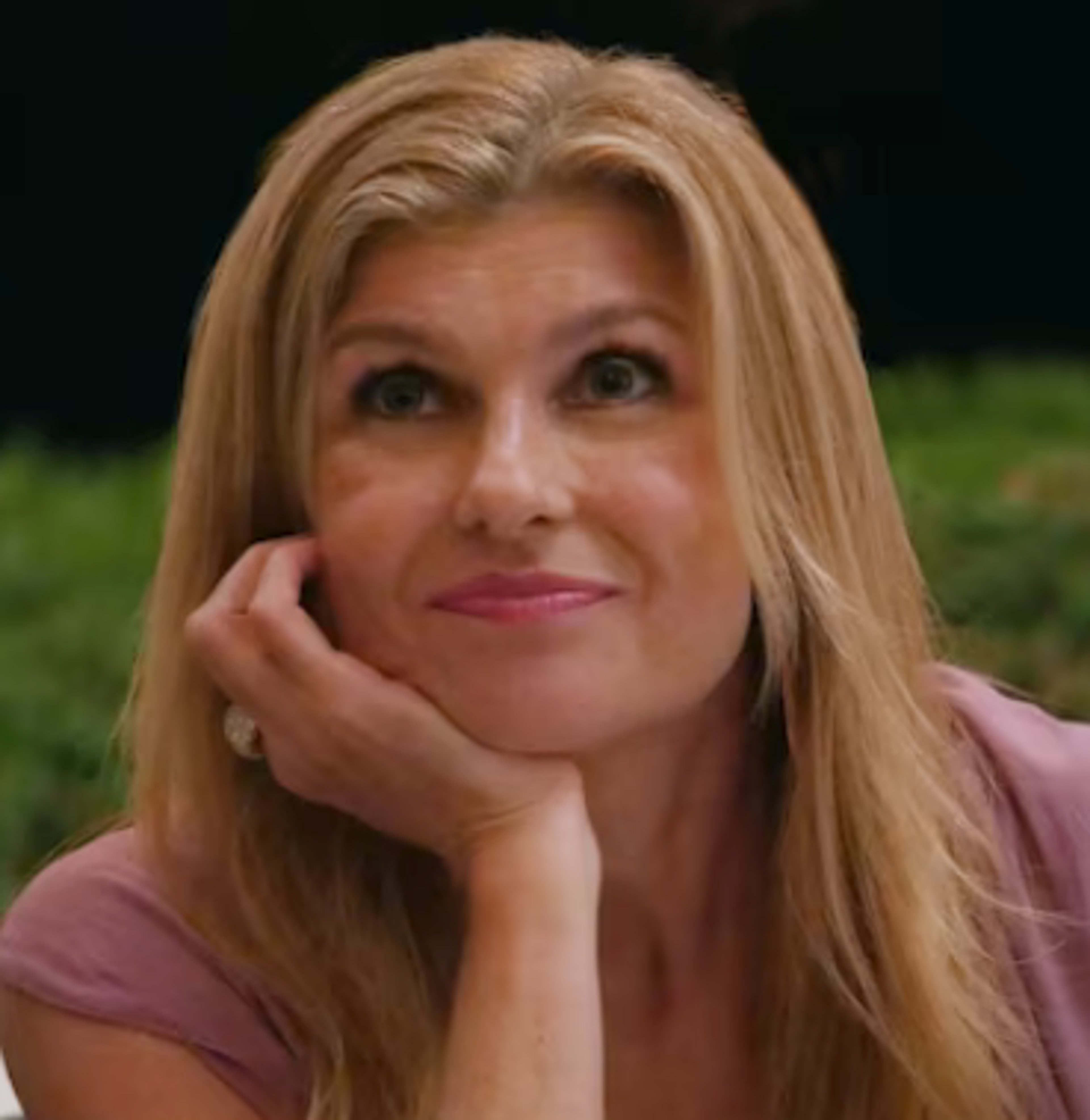 A middle-aged woman with blonde hair and a pink top looking directly at the camera with a confident expression.