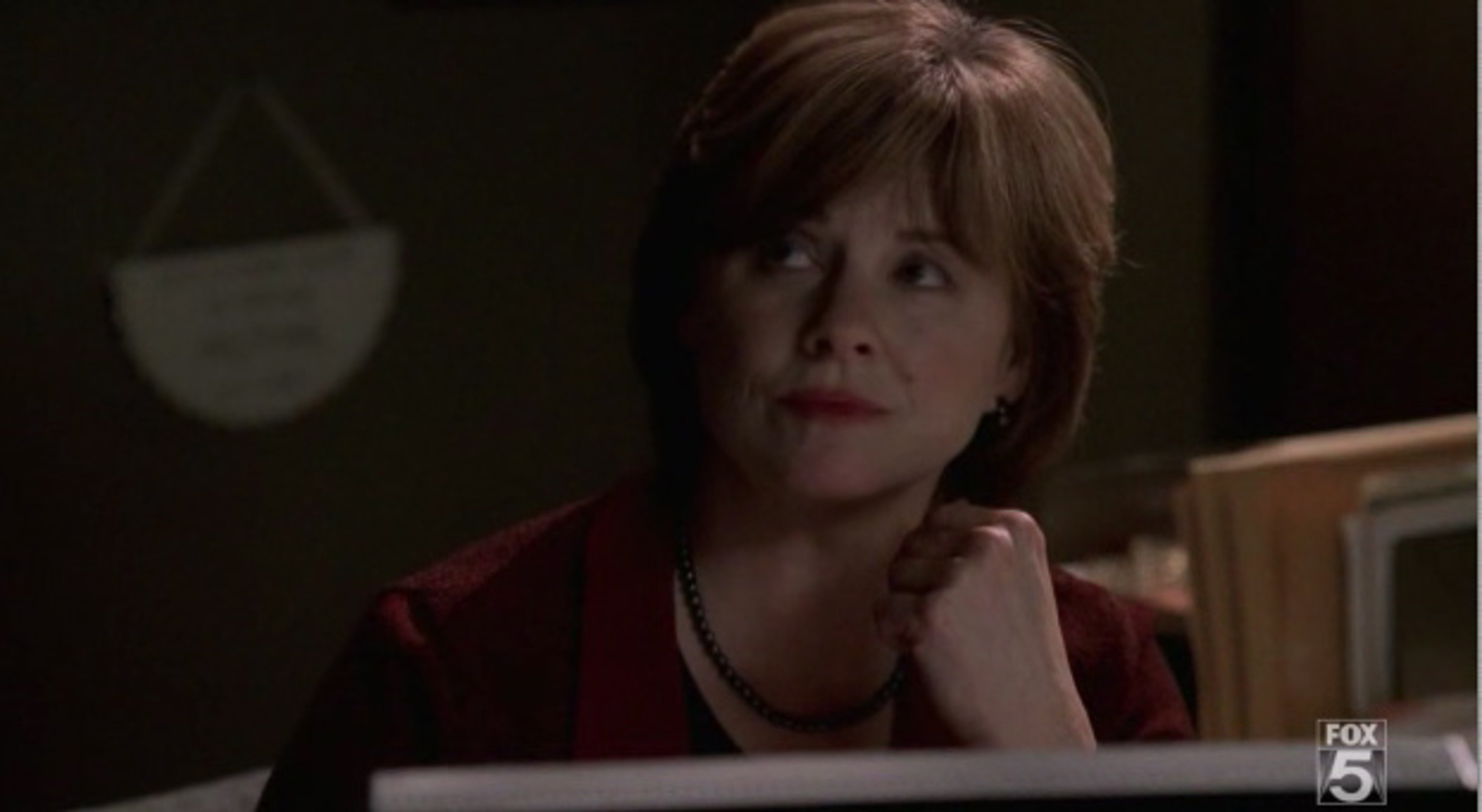 A middle-aged woman with short brown hair wearing a red blazer sitting at a desk or table