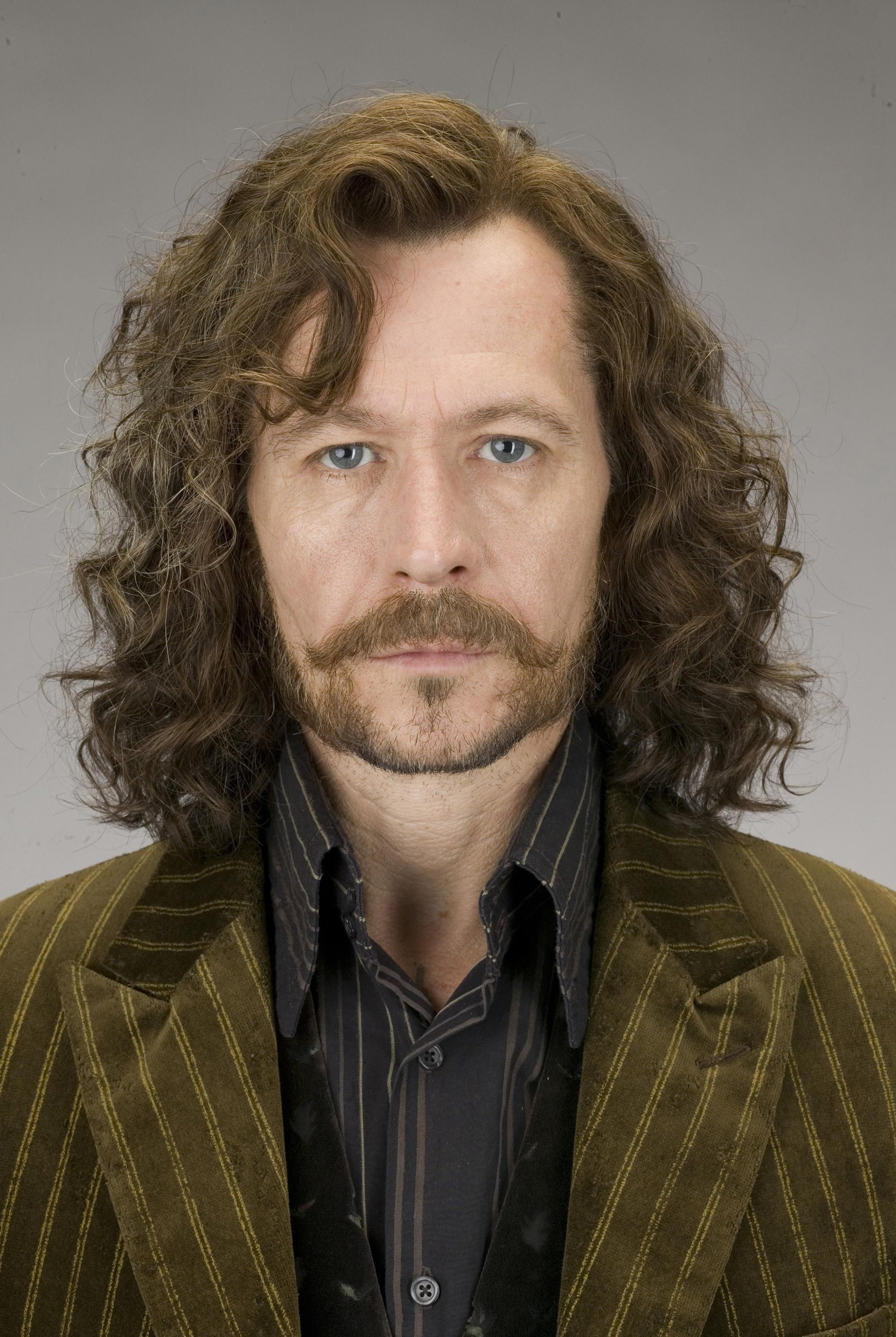 A man with long, curly dark hair and a beard wearing a green and black striped jacket