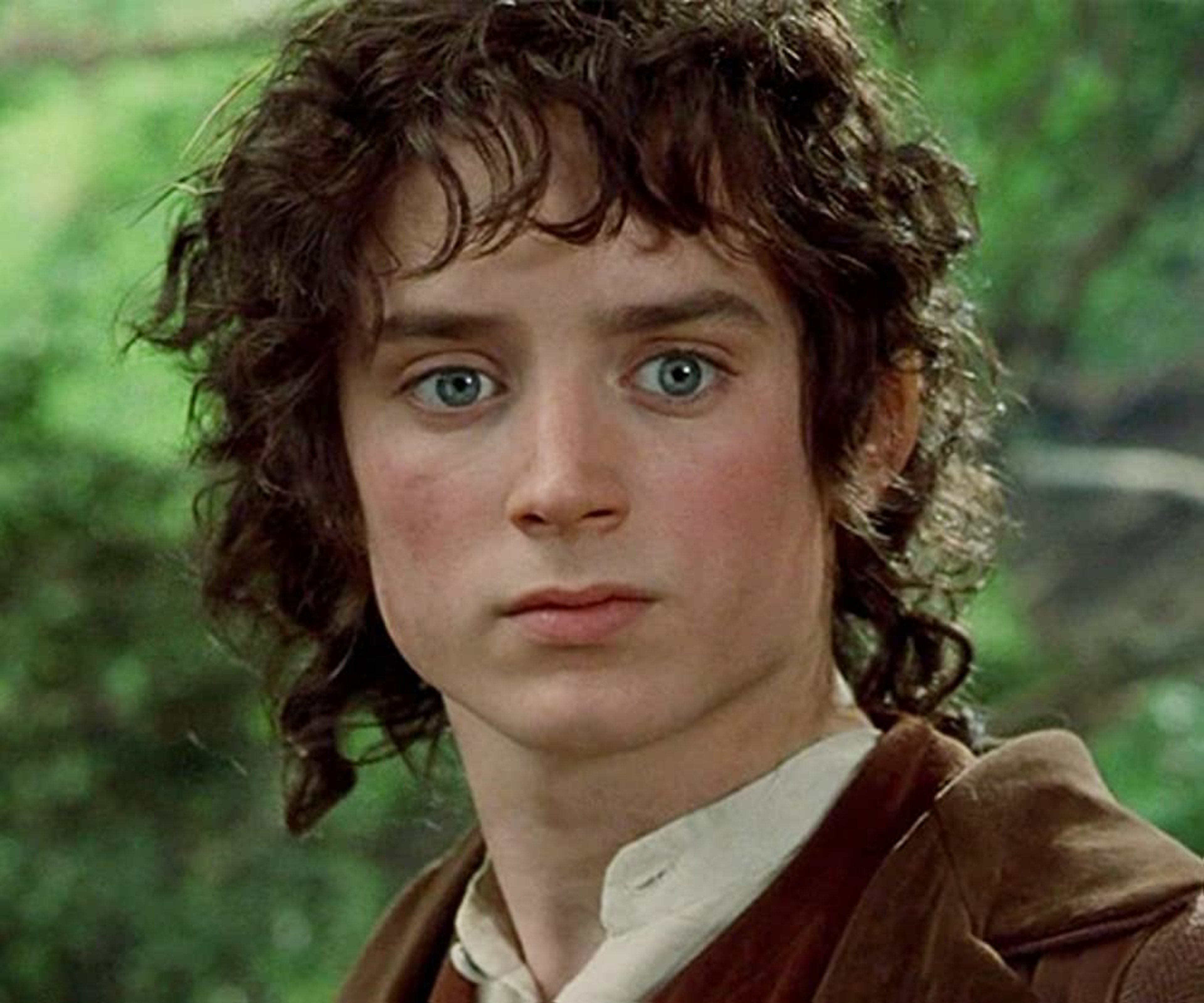 A young man with curly brown hair and green eyes, wearing a light-colored shirt or tunic.